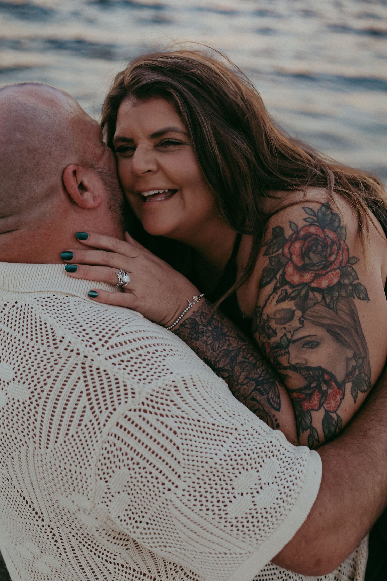 A couple sharing an intimate moment by the water at sunset while wearing a white crochet top.