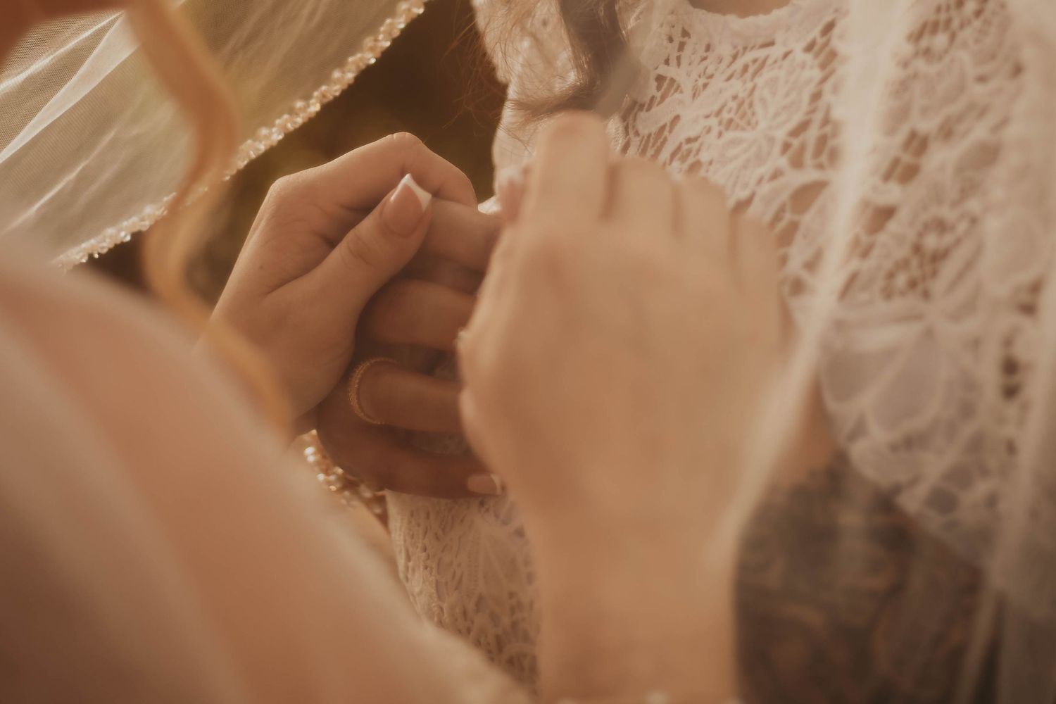 A bride in a white lace dress stands gracefully against a soft, warm-toned background.