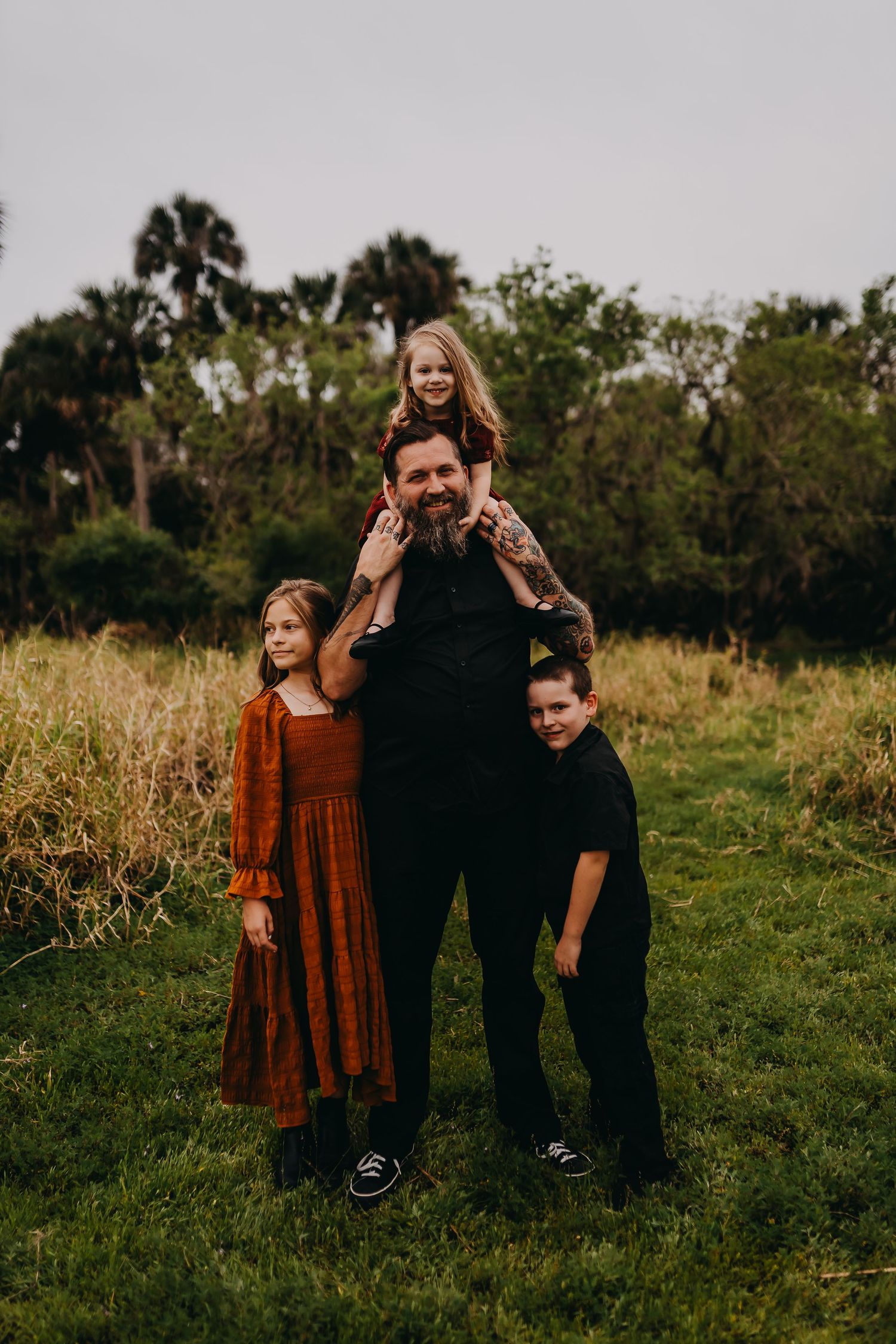 A family poses together in a grassy field with palm trees and greenery in the background.