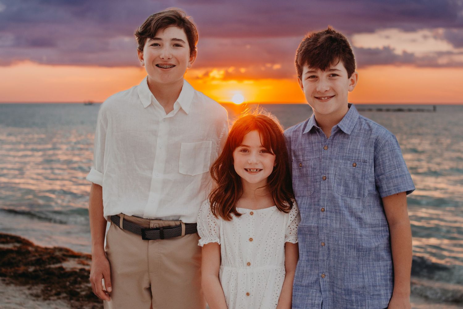 Family poses for sunset beach portraits in coordinating blue and white outfits along the ocean shore.
