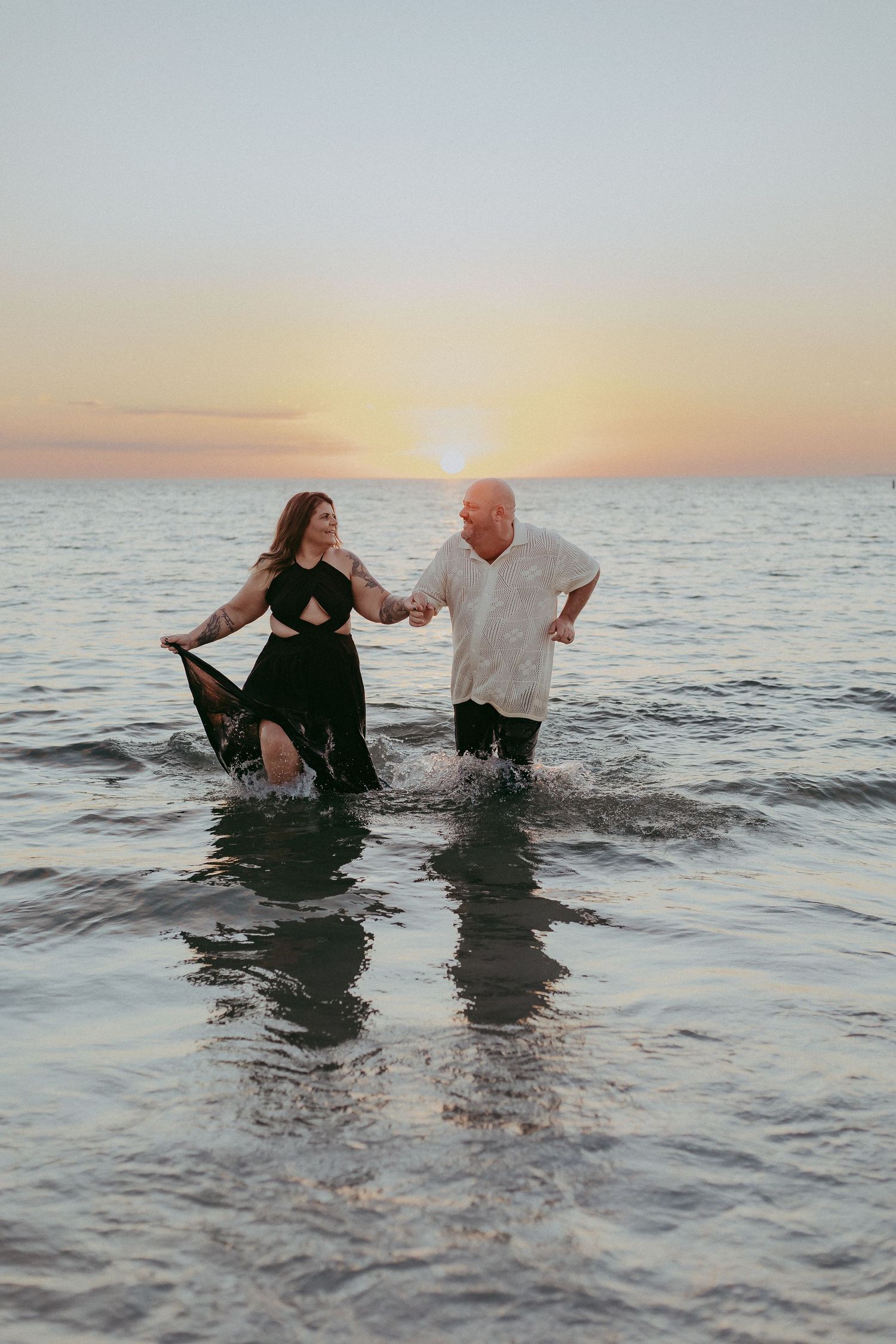 A couple splashes and plays together in the ocean water during sunset creating joyful moments at the beach.