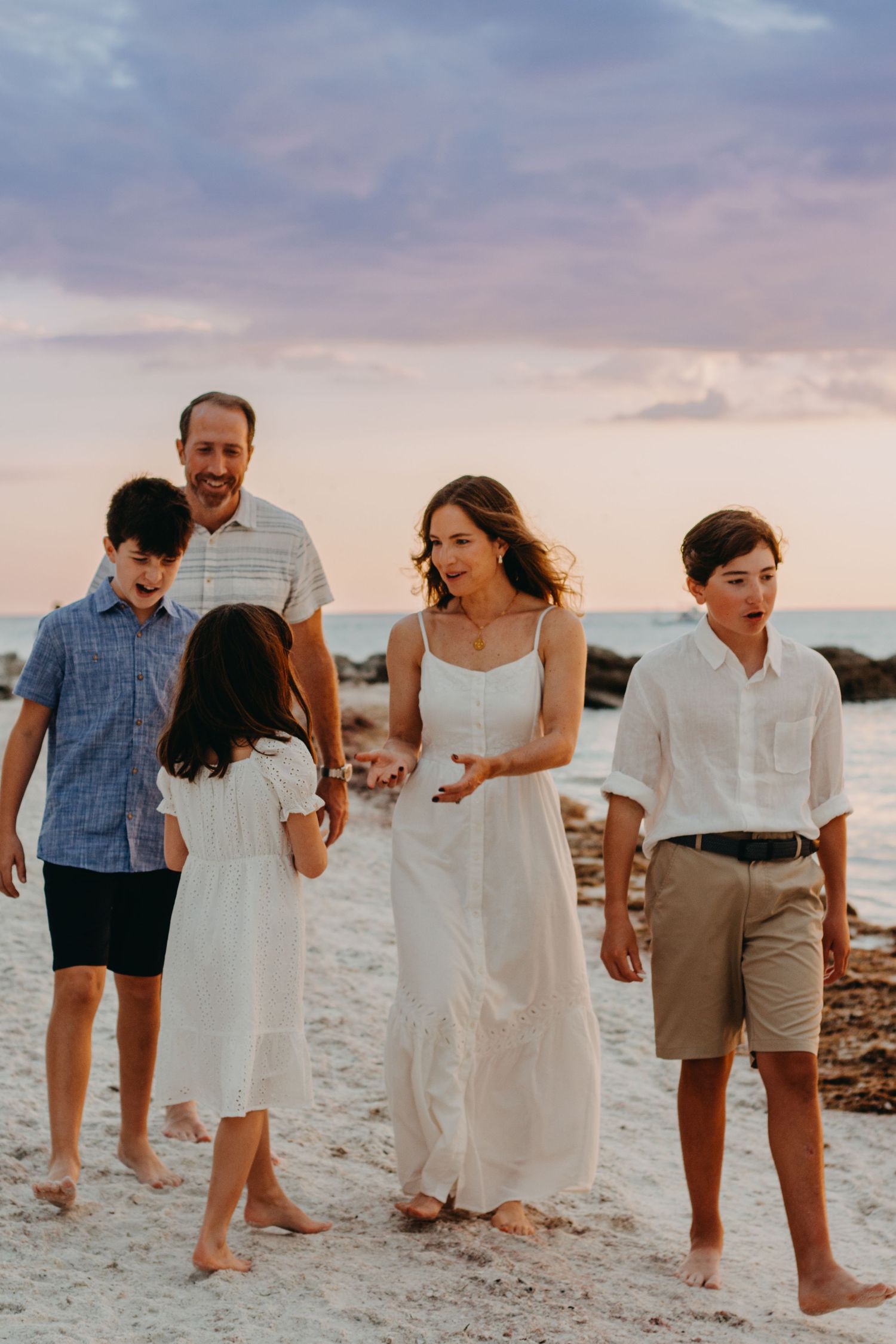 A group of people walking together on a white sandy beach at sunset wearing casual beach attire.