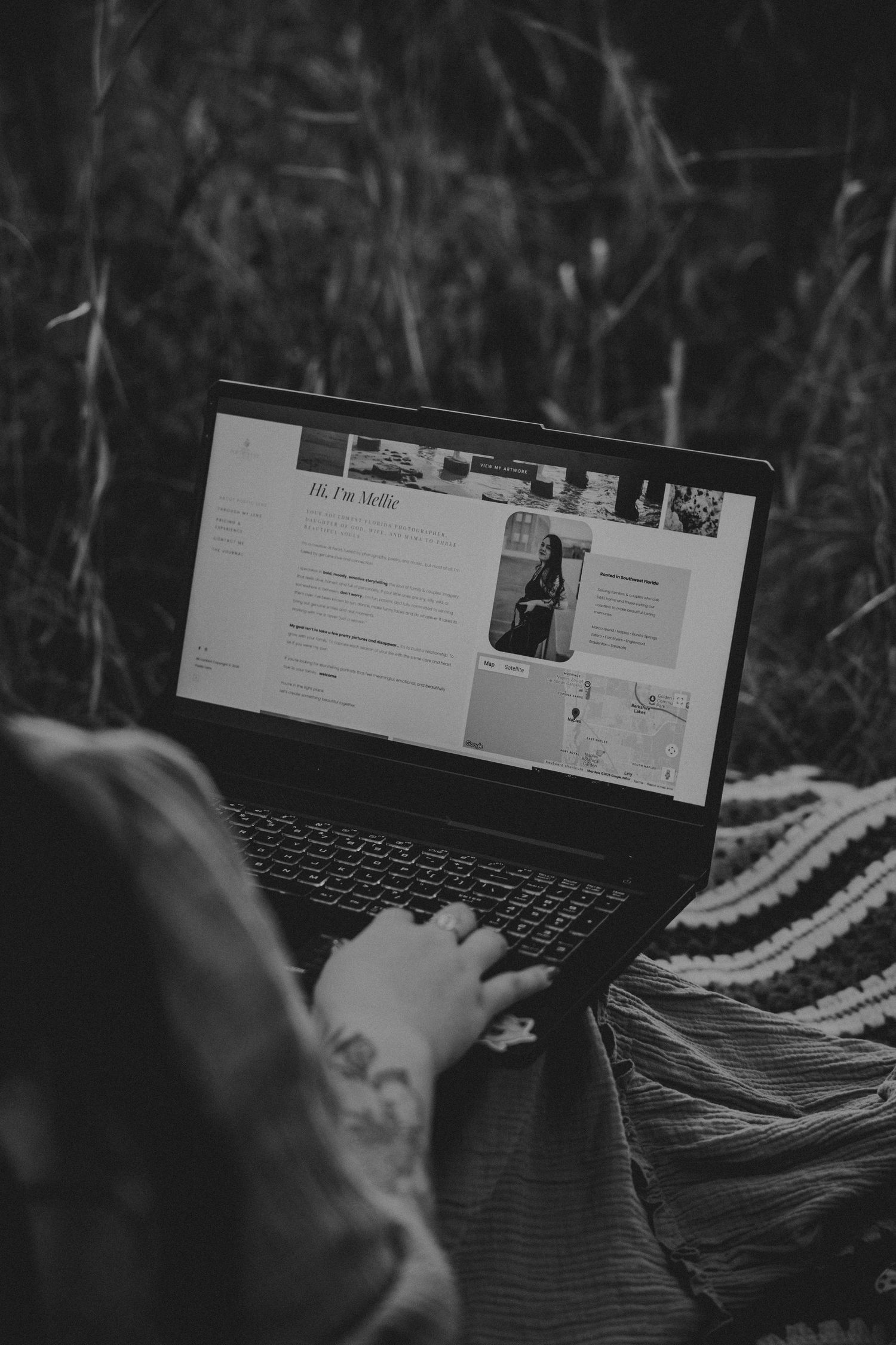 Black and white photo of person using laptop outdoors in grass, viewing a personal portfolio website.