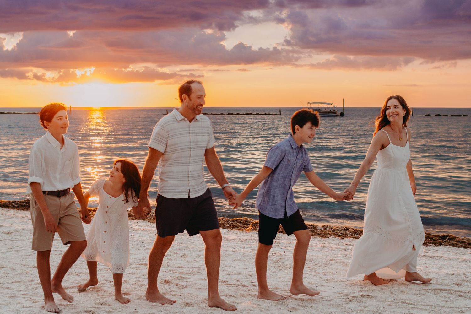 Silhouettes of people dancing in a line at sunset on a beach with golden light reflecting off the ocean waves.