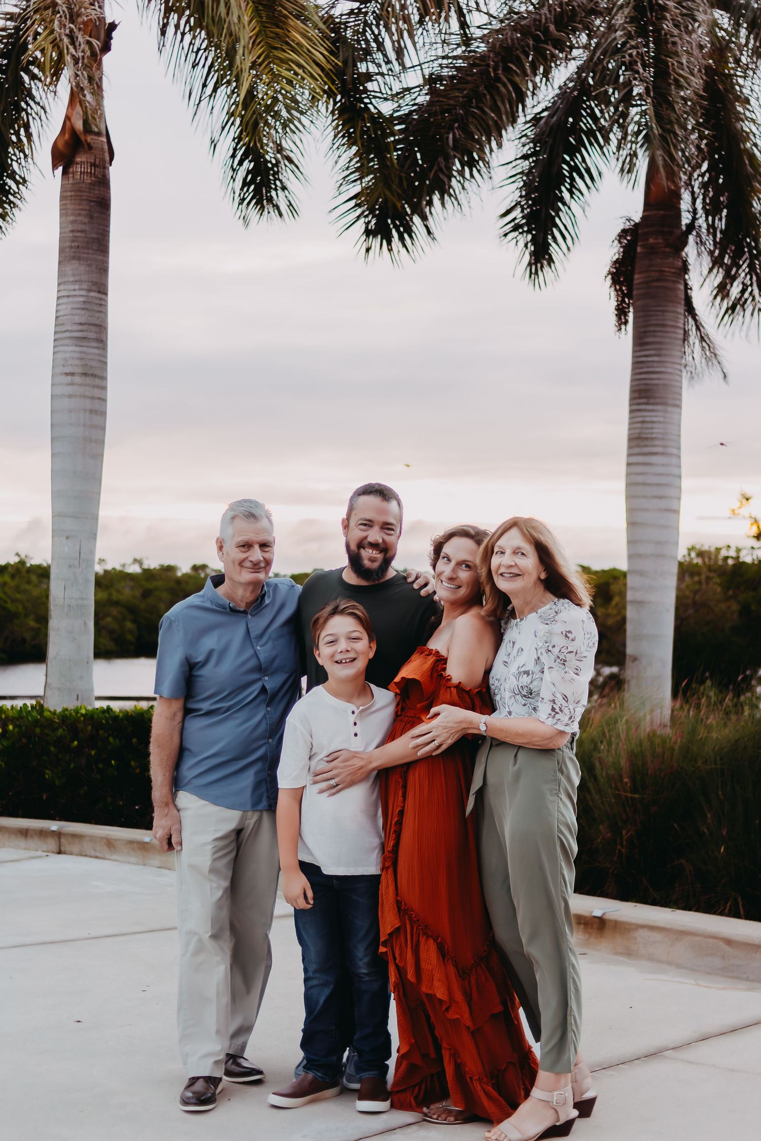 A group poses together on a white patio with palm trees at sunset in a casual outdoor setting.