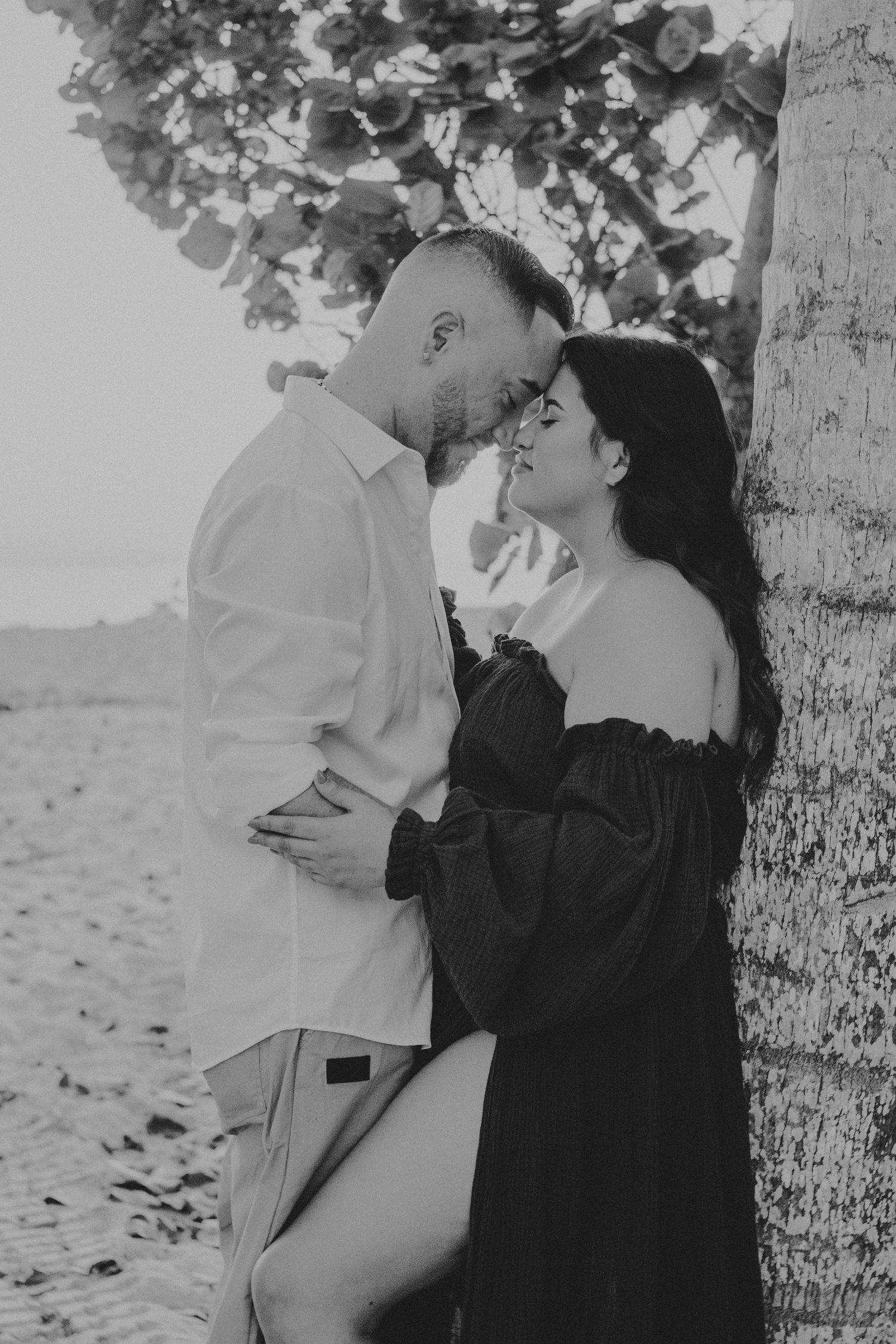 A vintage black and white photo series showing a romantic couple embracing against a tree in silhouette.