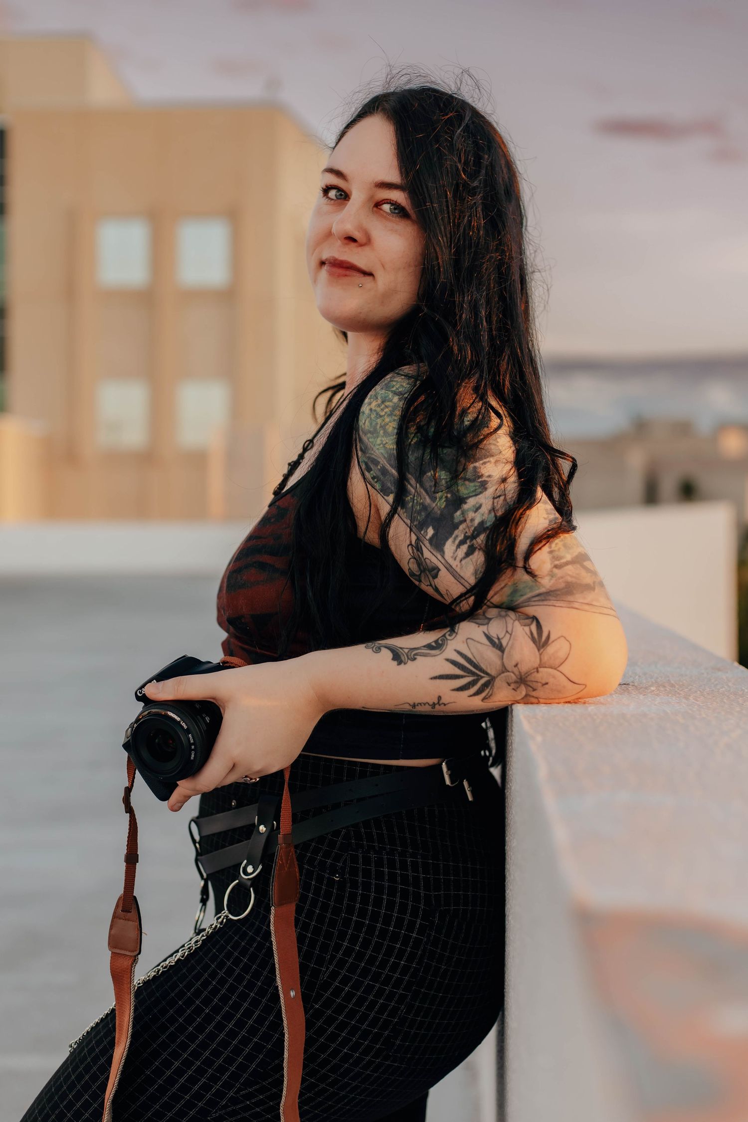 A woman in a black dress poses against a beige wall during golden hour sunset lighting.