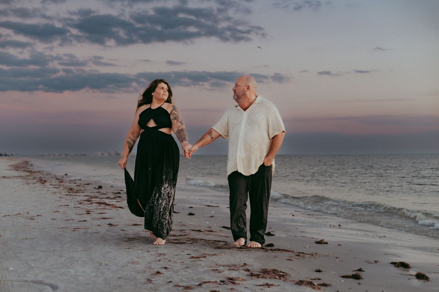 A couple walks along a scenic beach at sunset, holding hands and enjoying the peaceful coastal atmosphere.