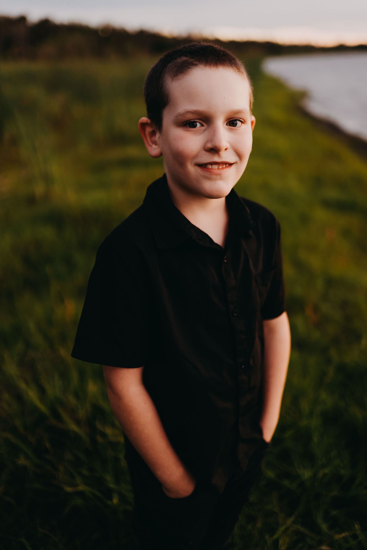 Child in black t-shirt smiling at sunset in grassy field with warm lighting.
