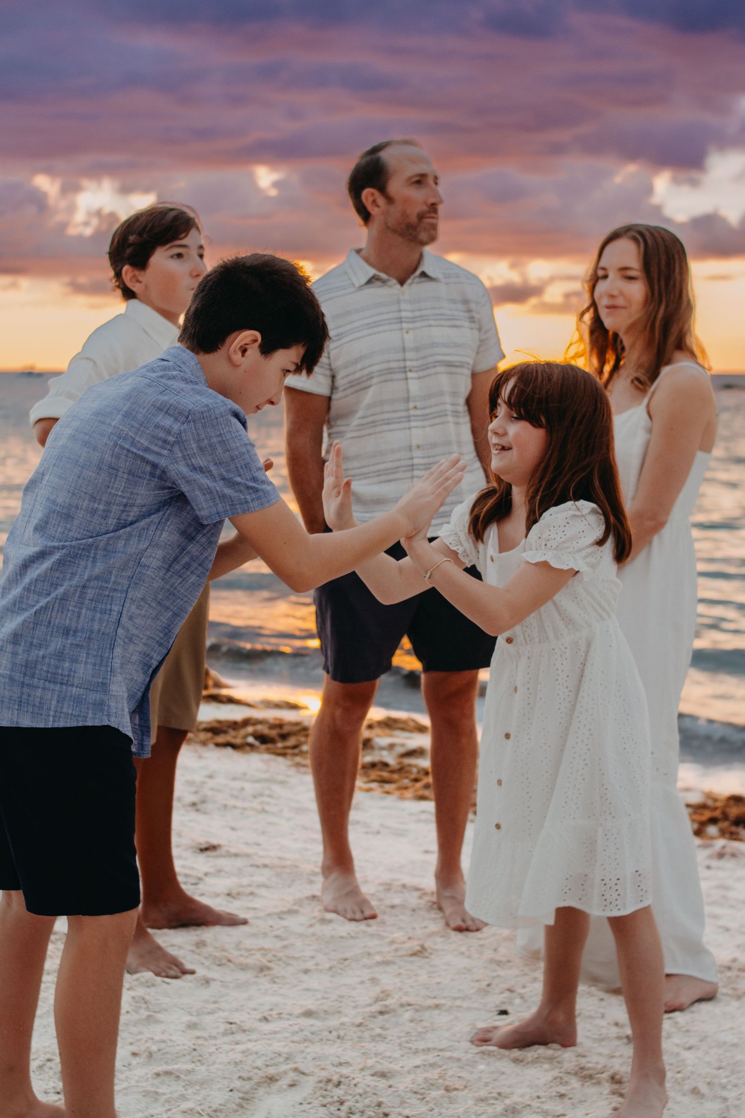 Family enjoying a playful moment together on the beach at sunset with dramatic orange and purple sky.