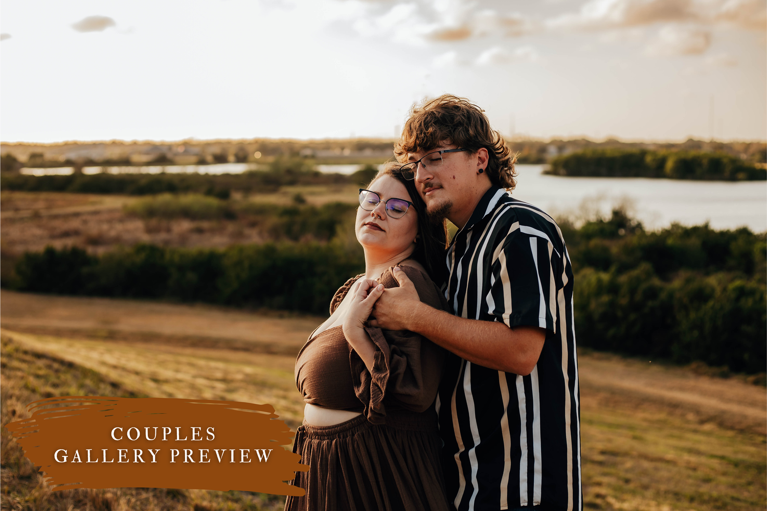 A couple in casual attire embraces while standing in a golden field during sunset.