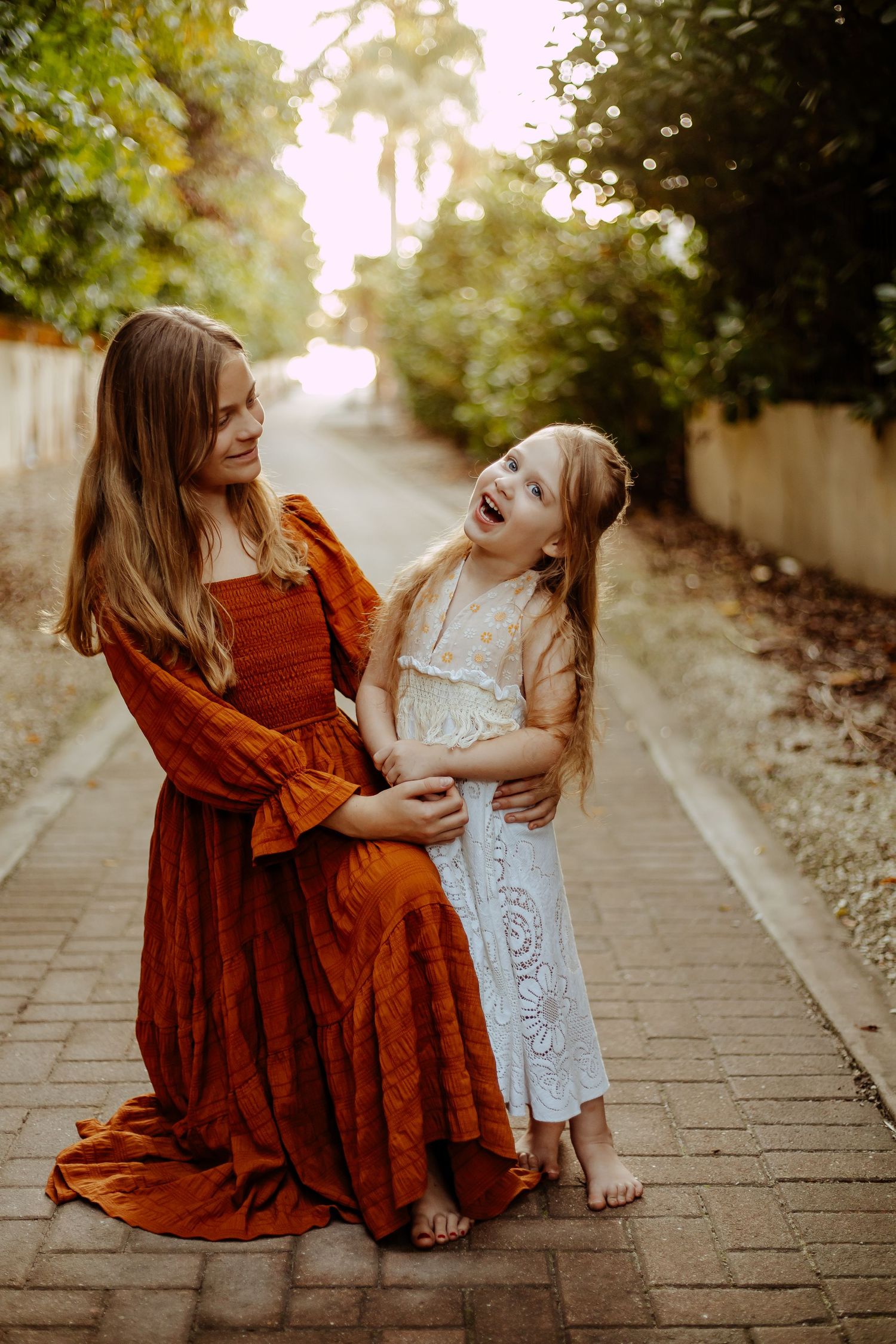 A parent and child share a joyful moment sitting together on a brick pathway surrounded by greenery.