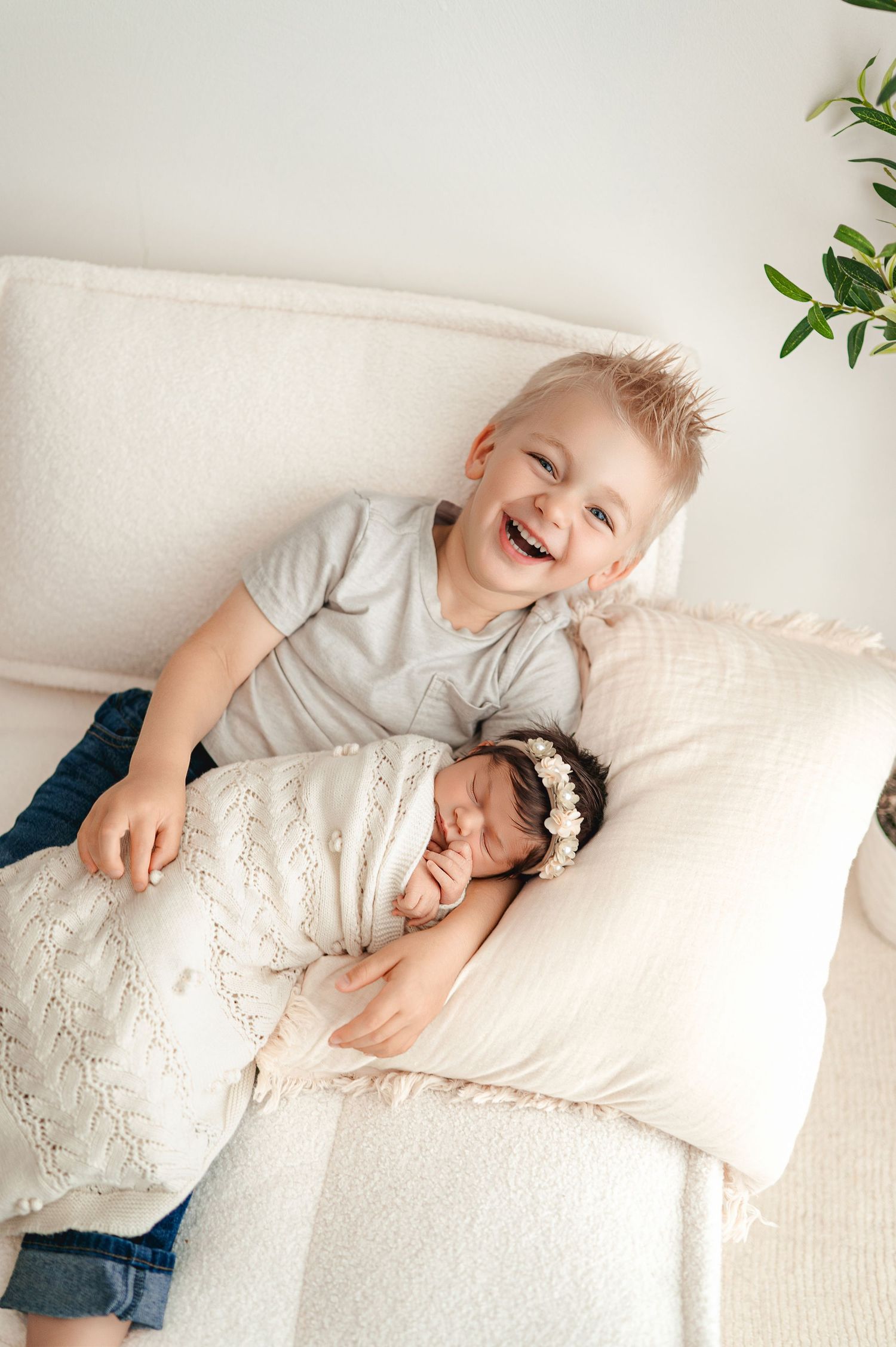 Young siblings share sweet laughter and playful moments while lying on white textured blanket.