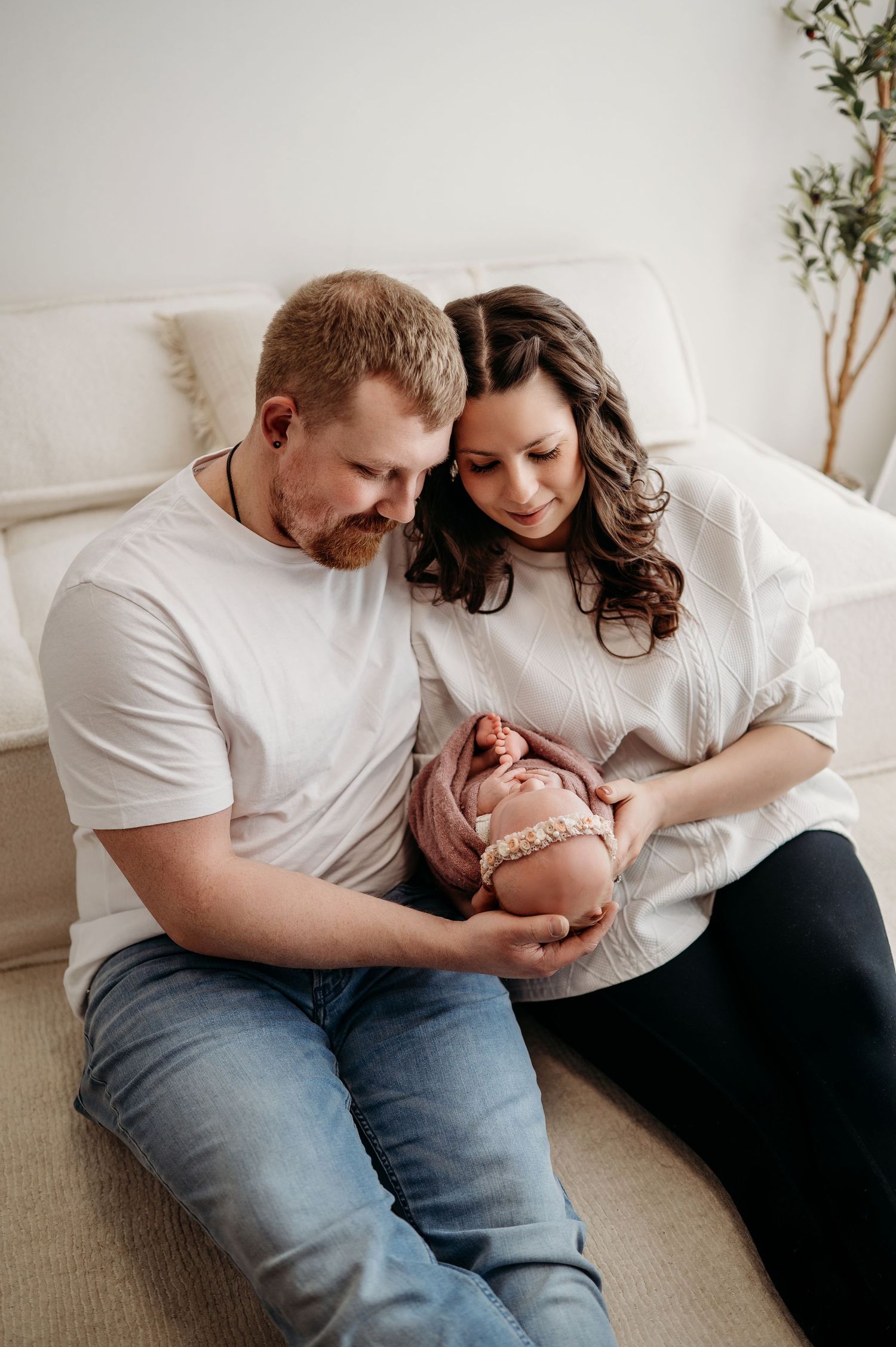 A cozy family moment on a white couch as parents share an intimate moment with their newborn child.