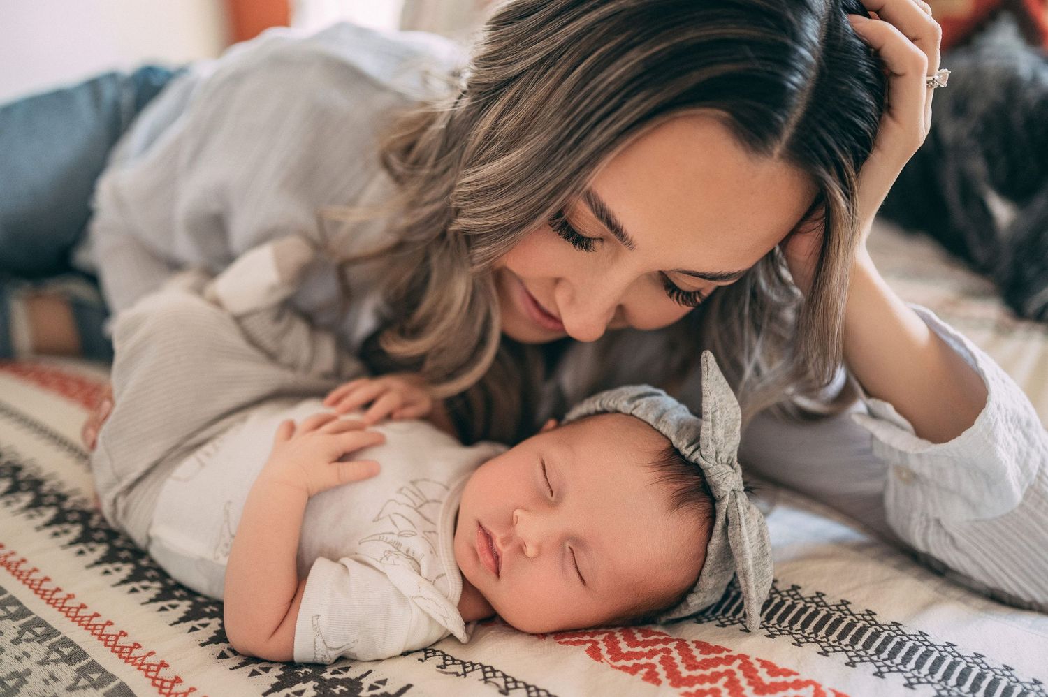 A gentle moment of bonding with a sleeping newborn on a patterned blanket.