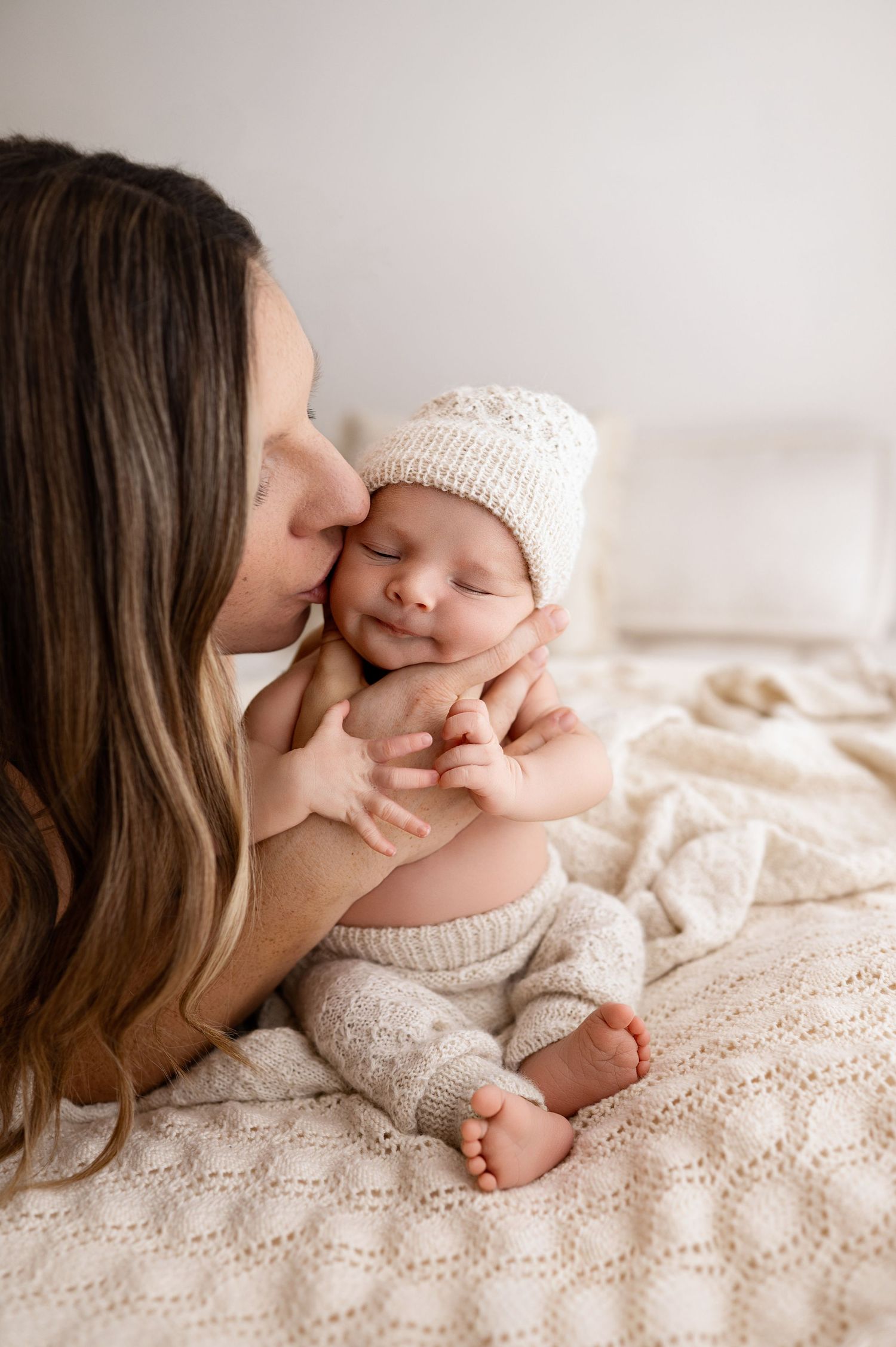 Tender moment between parent and baby on cream knit blanket in natural light.