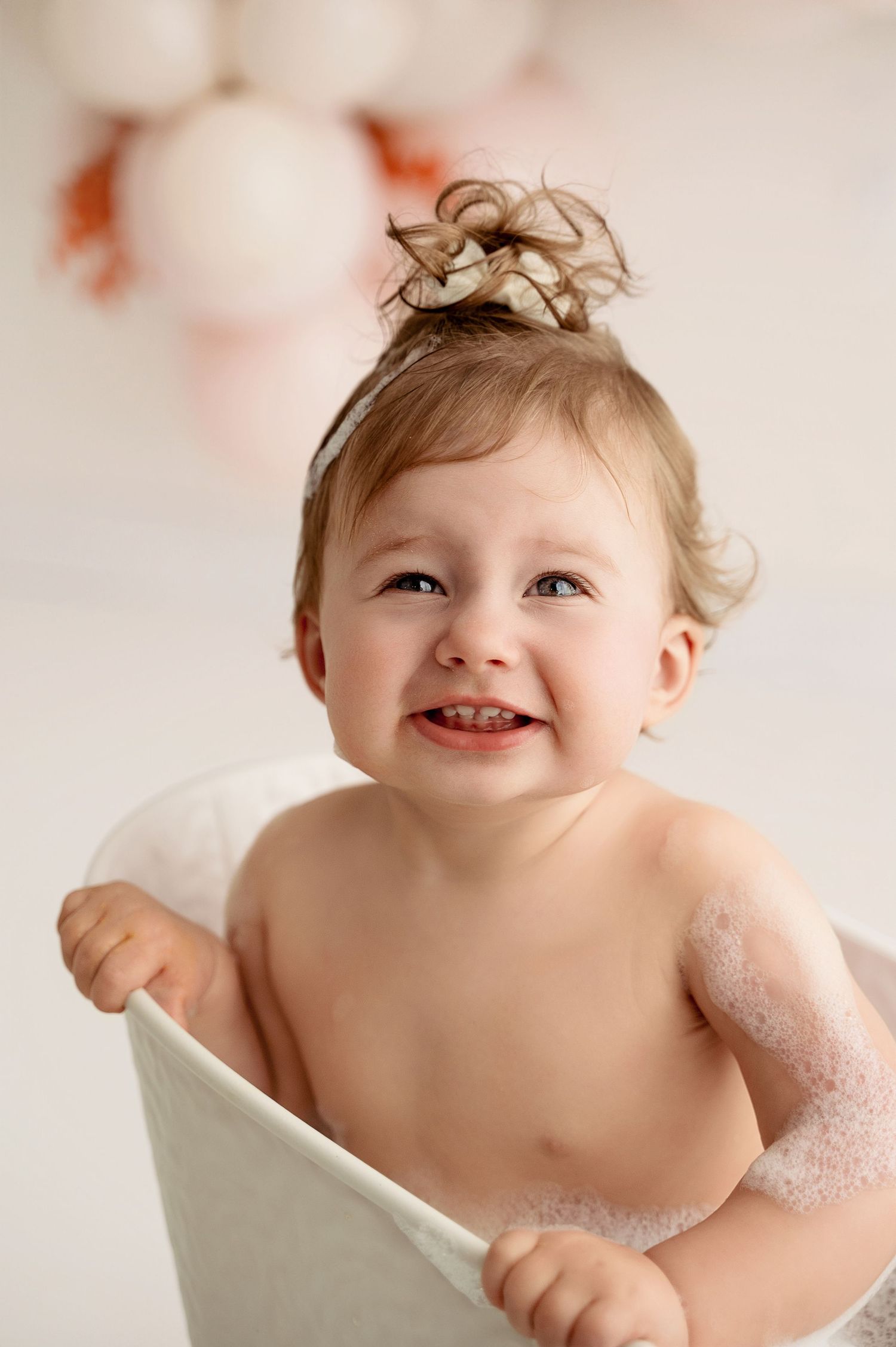 A happy baby sits in a white bathtub with bubbles during bath time, showing a joyful expression.