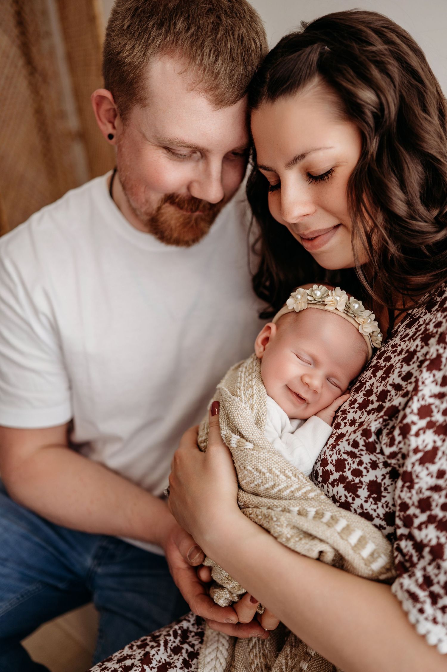 Sweet family portrait showing sleeping newborn in cream knit outfit with parents.