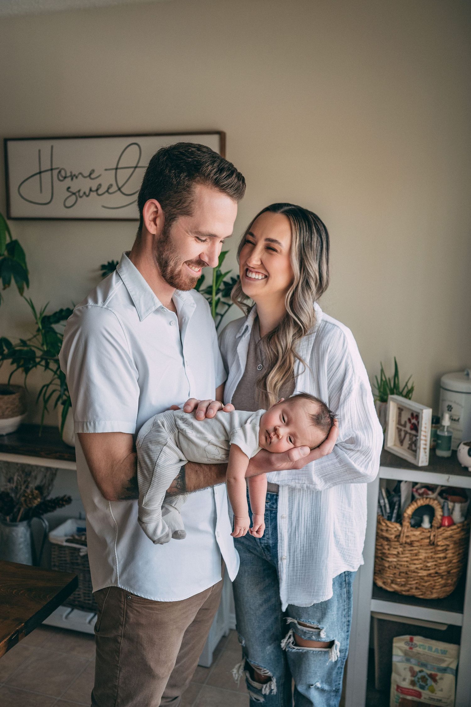 Family lifestyle portrait with newborn baby in casual white shirts against decorated wall.