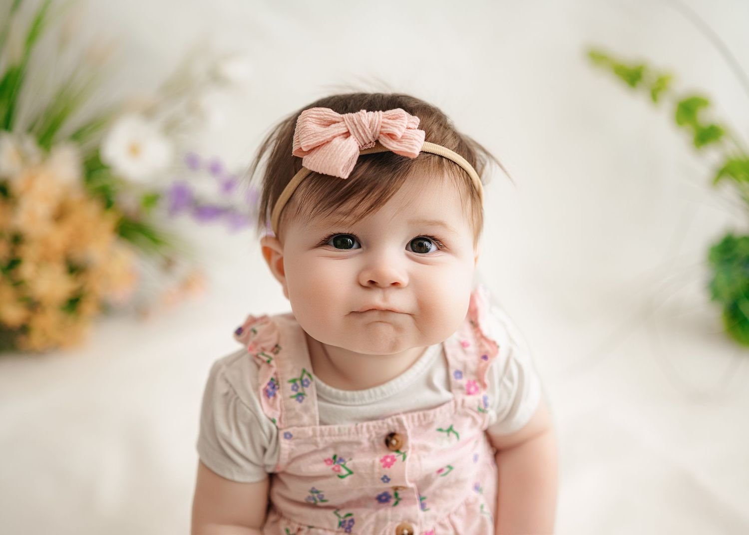 Professional studio photography series showing an infant wearing a floral dress against a soft beige backdrop.