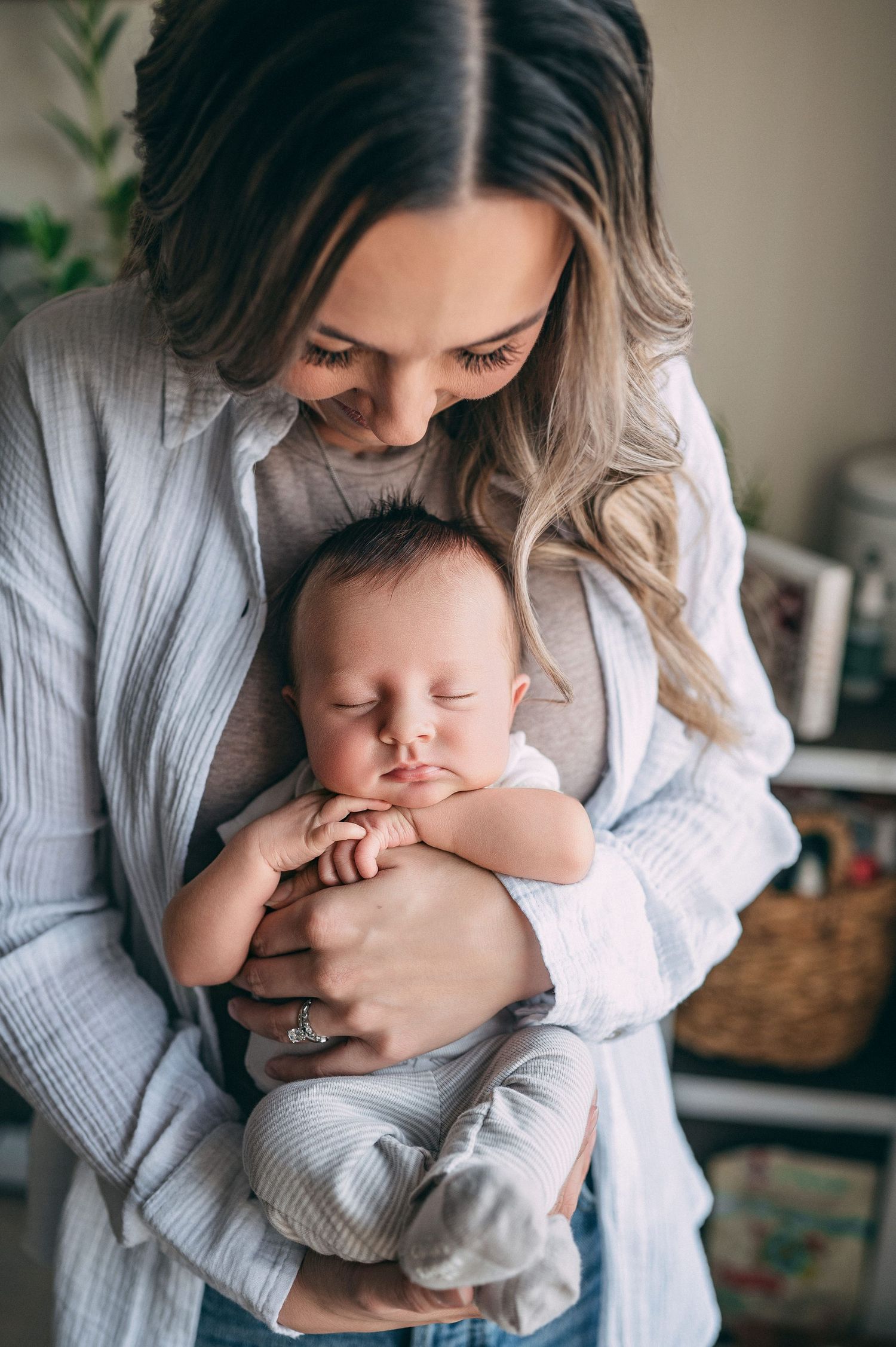 Tender moment as a parent holds sleeping newborn baby while wearing a cozy gray cardigan in a home setting.