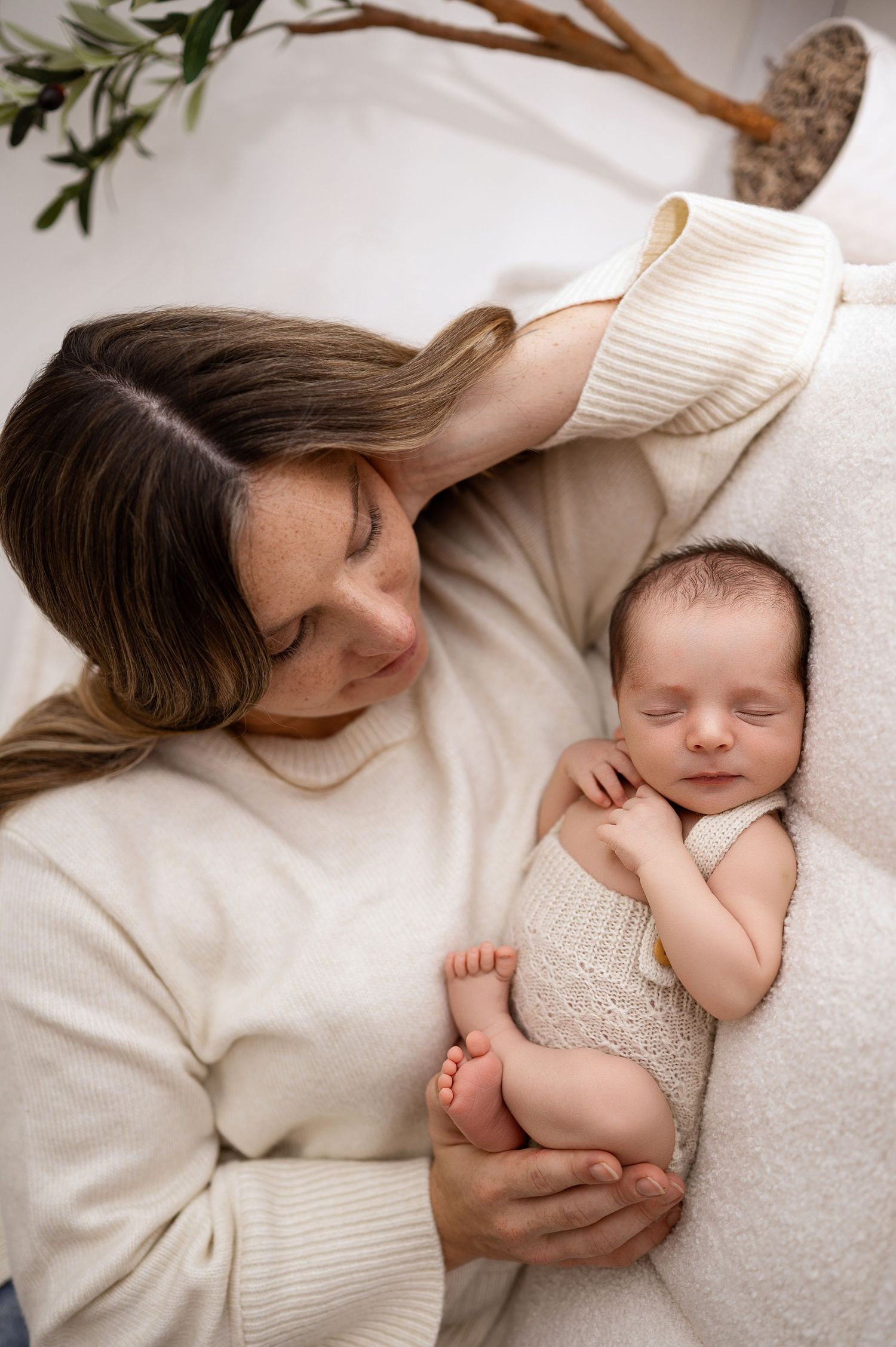 A tender moment captured in soft tones as parent and baby rest together on white bedding.