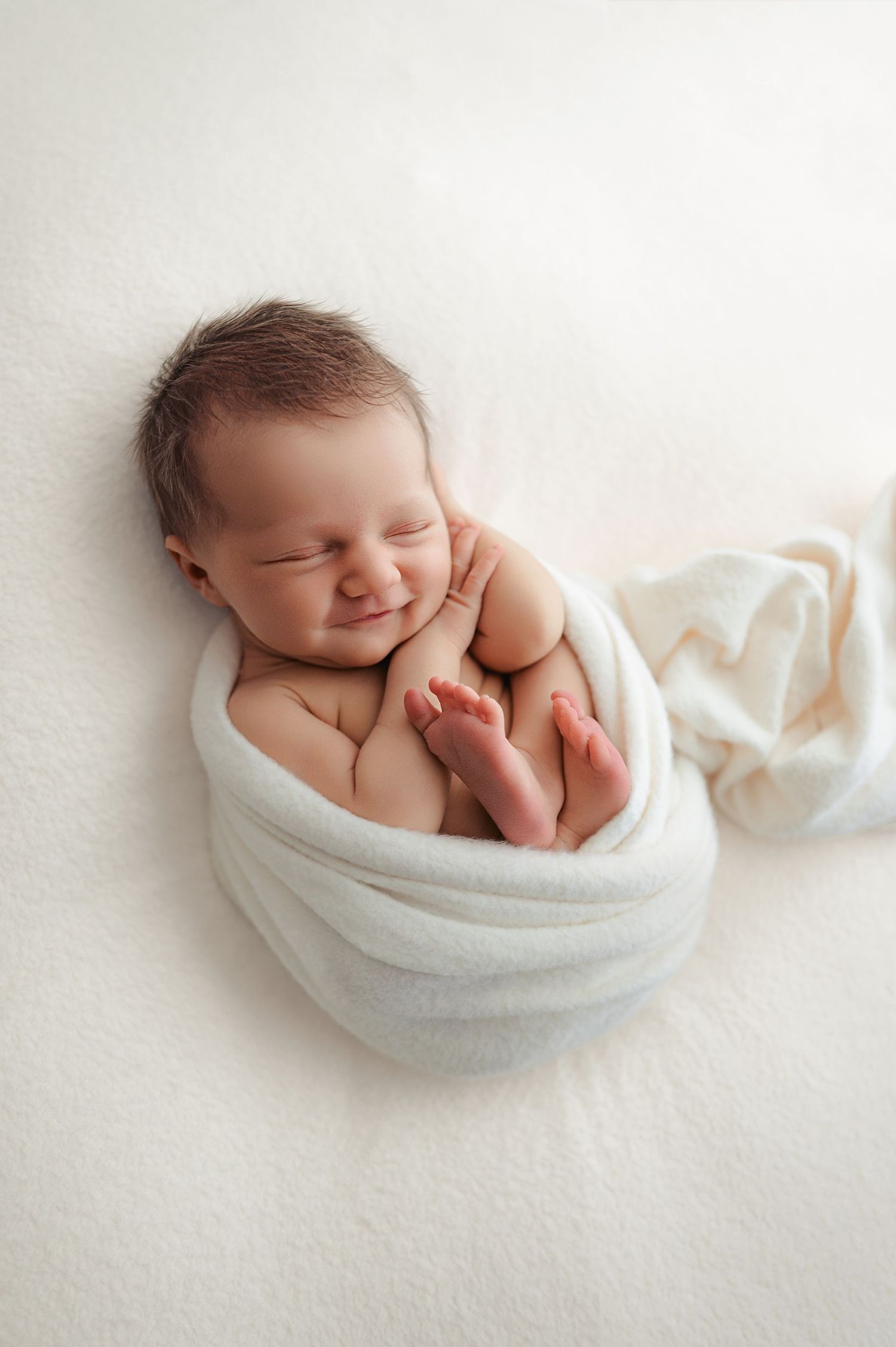 Peaceful sleeping newborn wrapped in soft white blanket on light background in minimalist style photography.