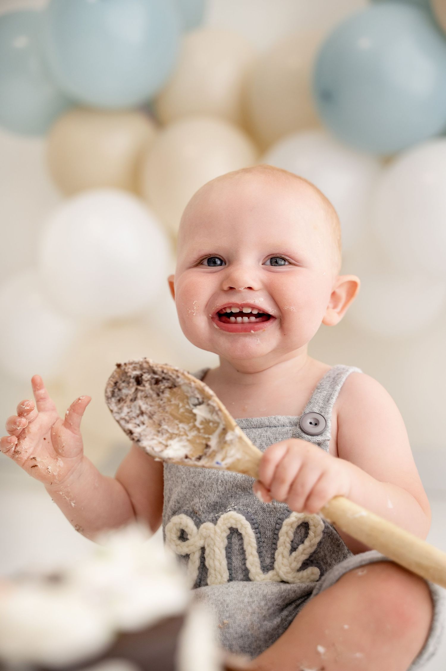A happy baby wearing grey clothing plays with flour or powdery ingredients while baking in a bright setting.
