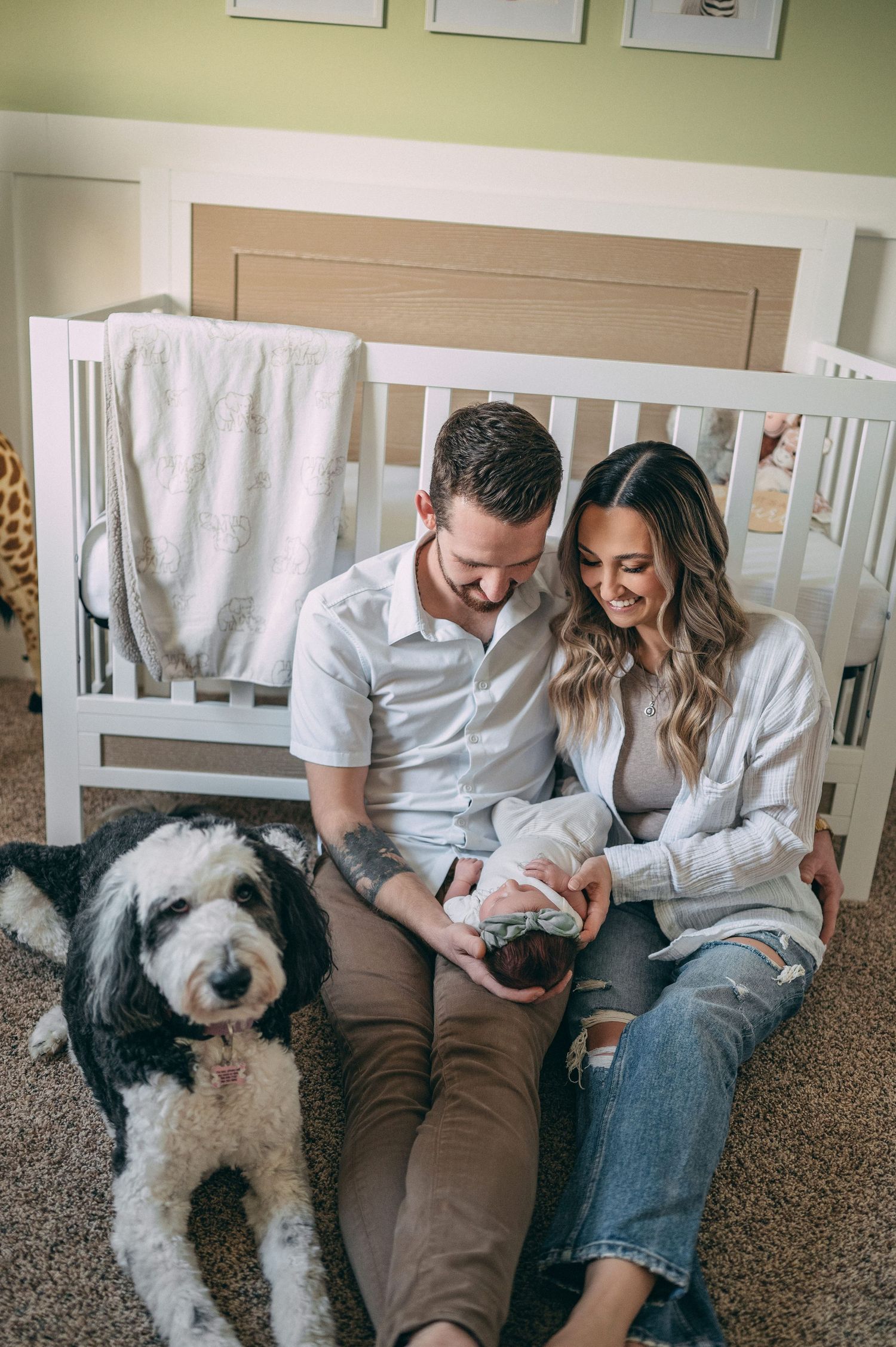 Family with fluffy dog relaxing by white crib in nursery room.