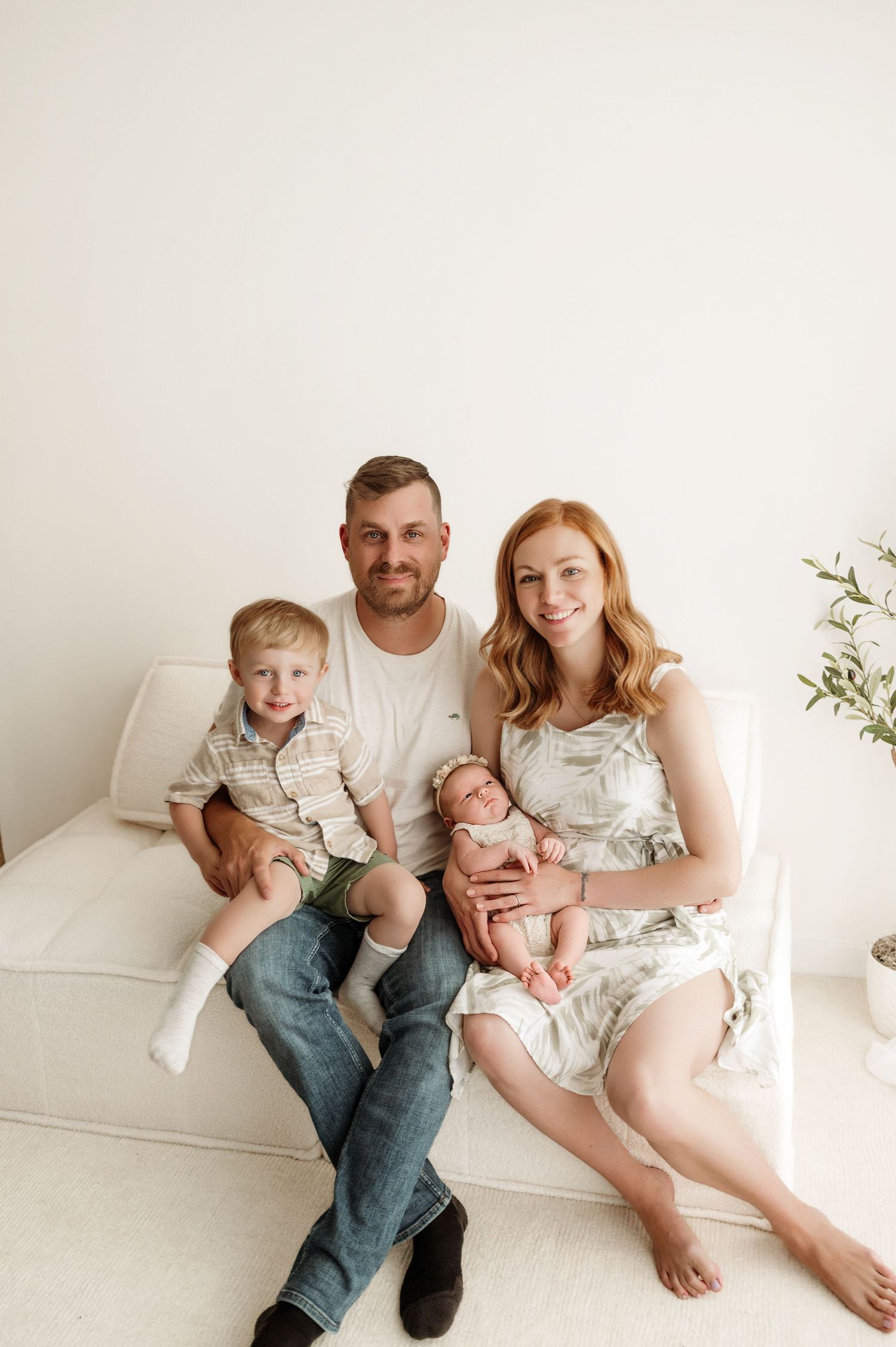 A family sits together on a white couch in a minimalist room with soft natural lighting.