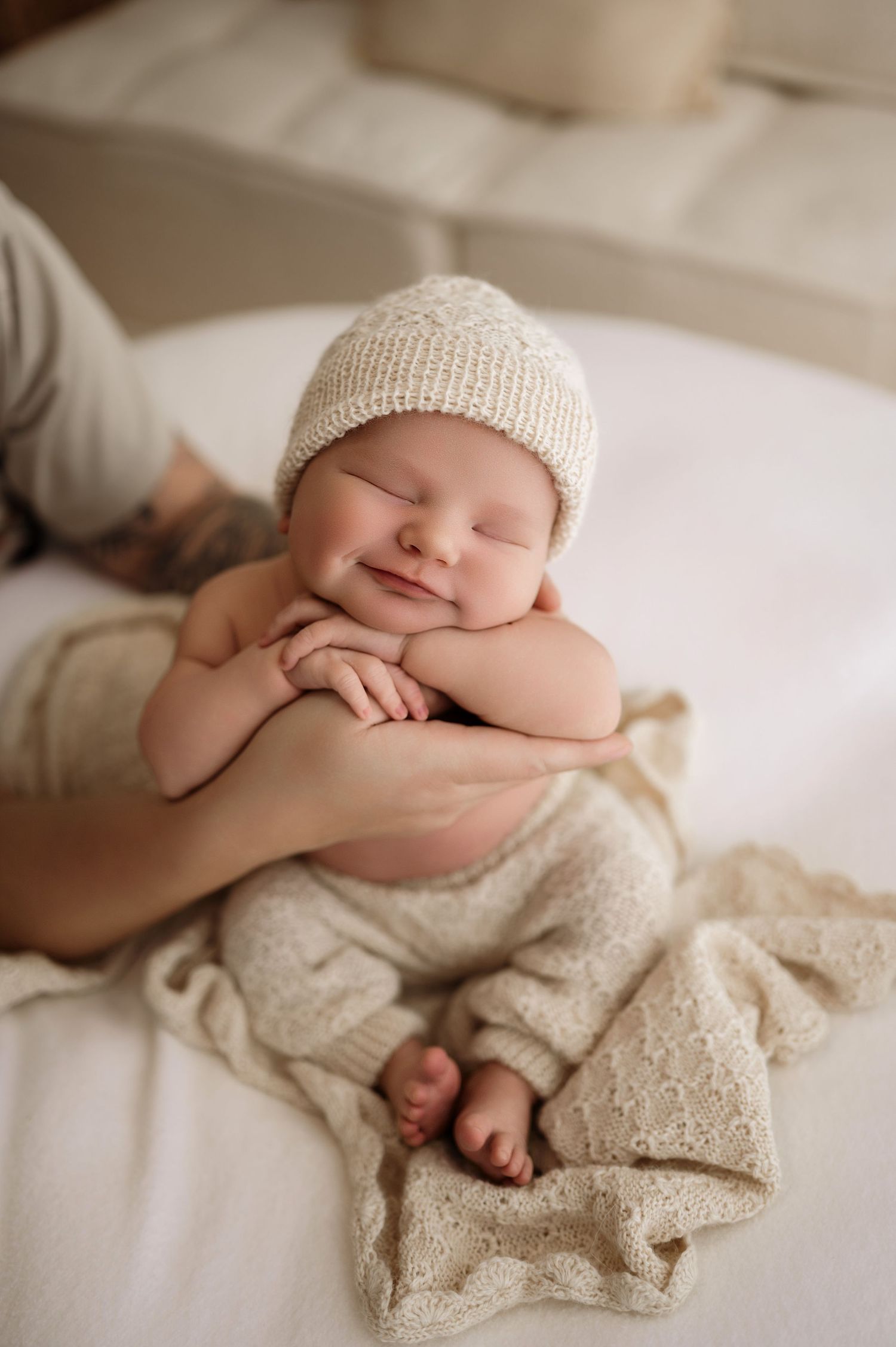 A sleeping baby wears a cream knit hat and lies on white textiles in a series of dreamy artistic newborn photographs.