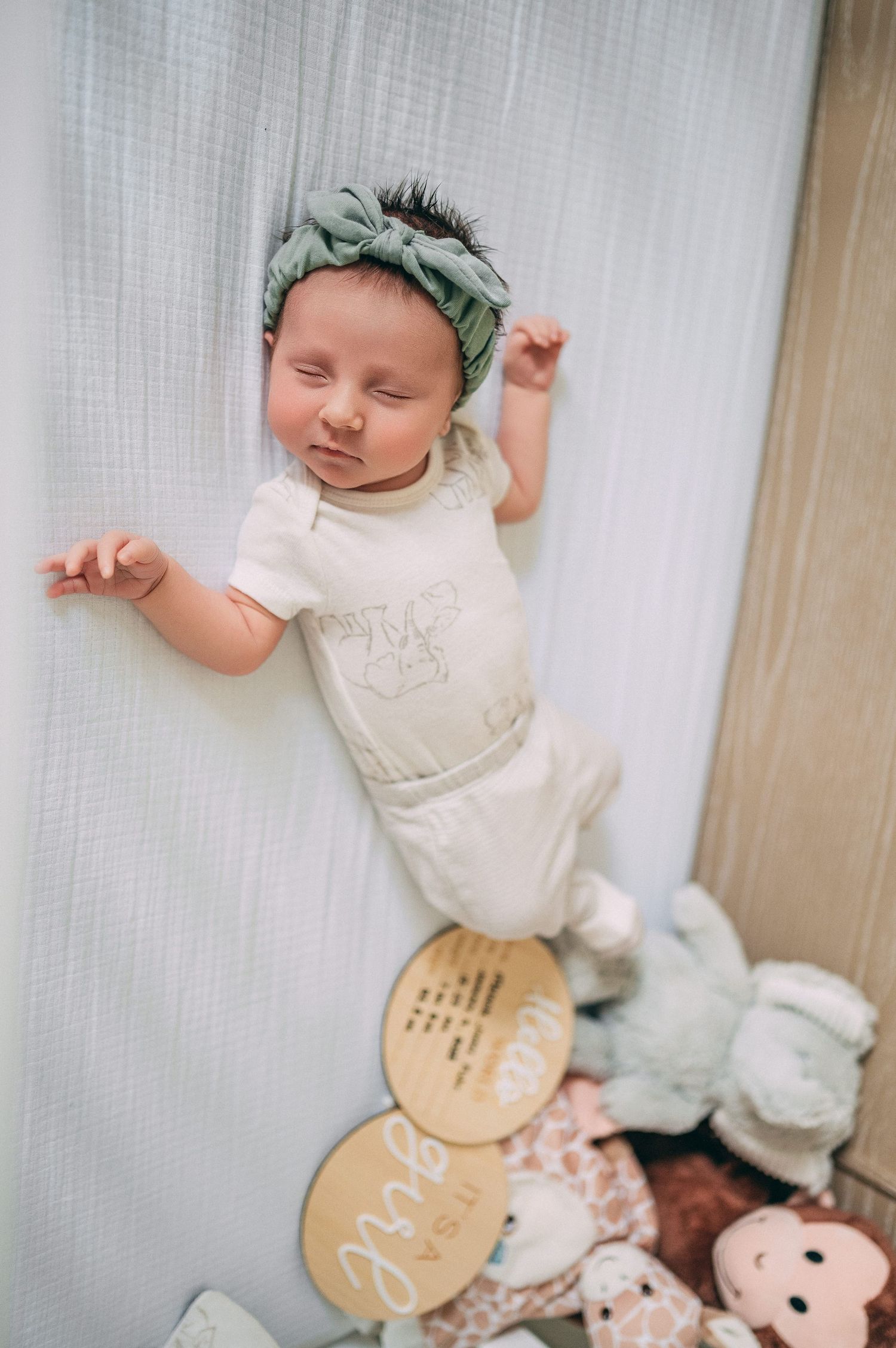 A sleeping newborn wearing a mint bow headband and white outfit lying on a light backdrop with decorative circles.
