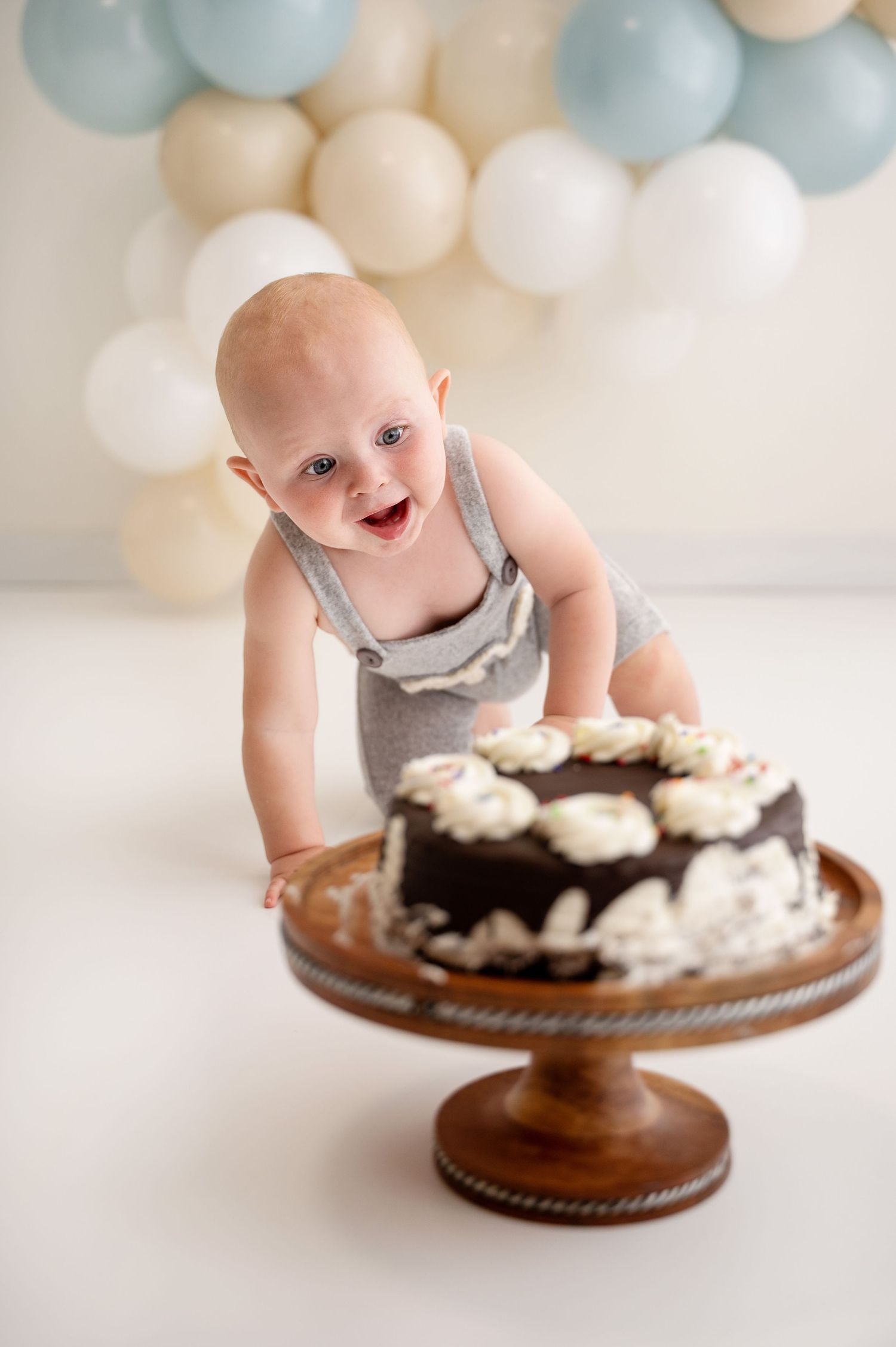 Baby reaching for cake on wooden cake stand with balloon decorations.
