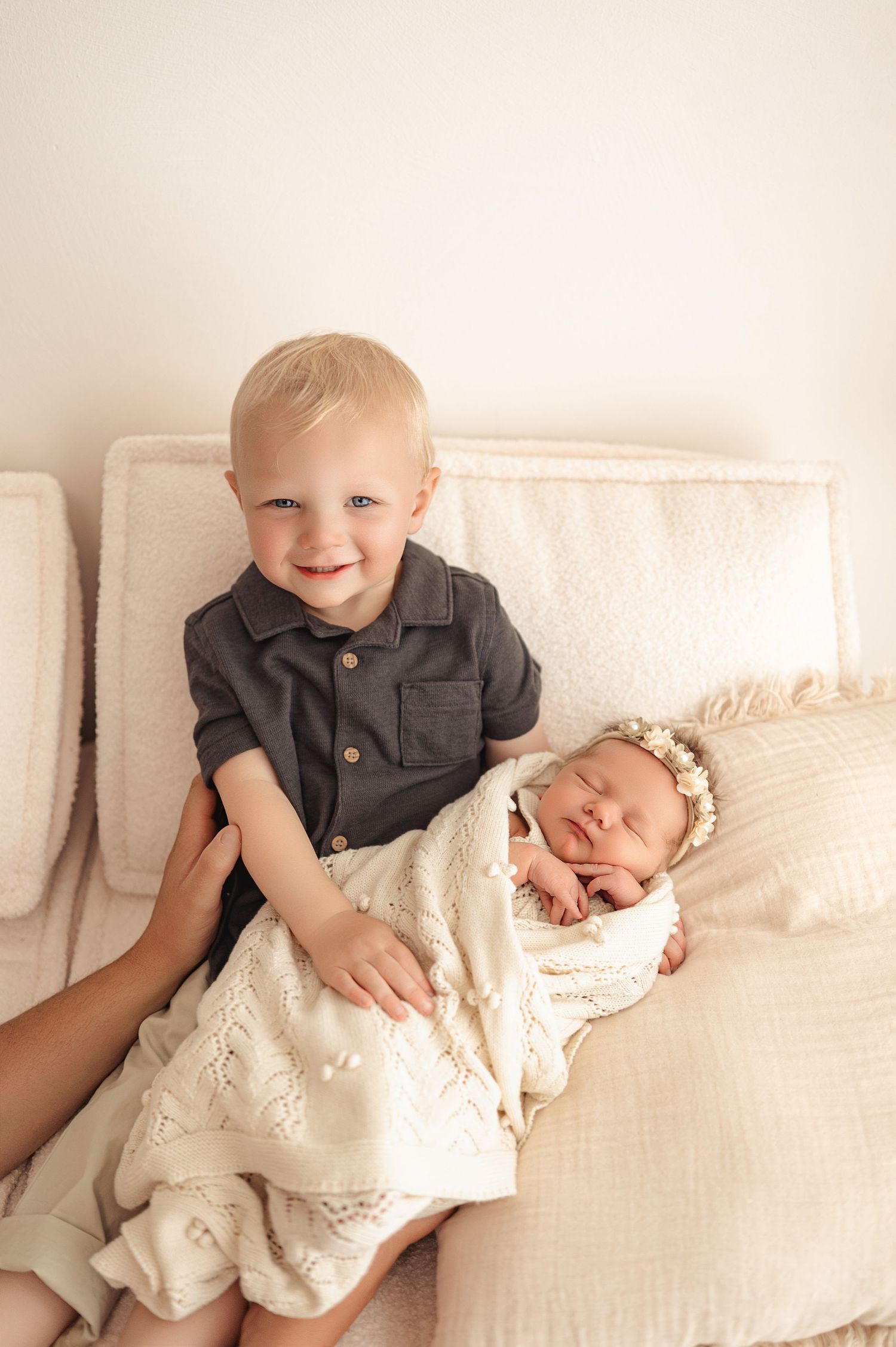 Sibling photo series showing tender moments between older child and newborn on white couch and blankets.