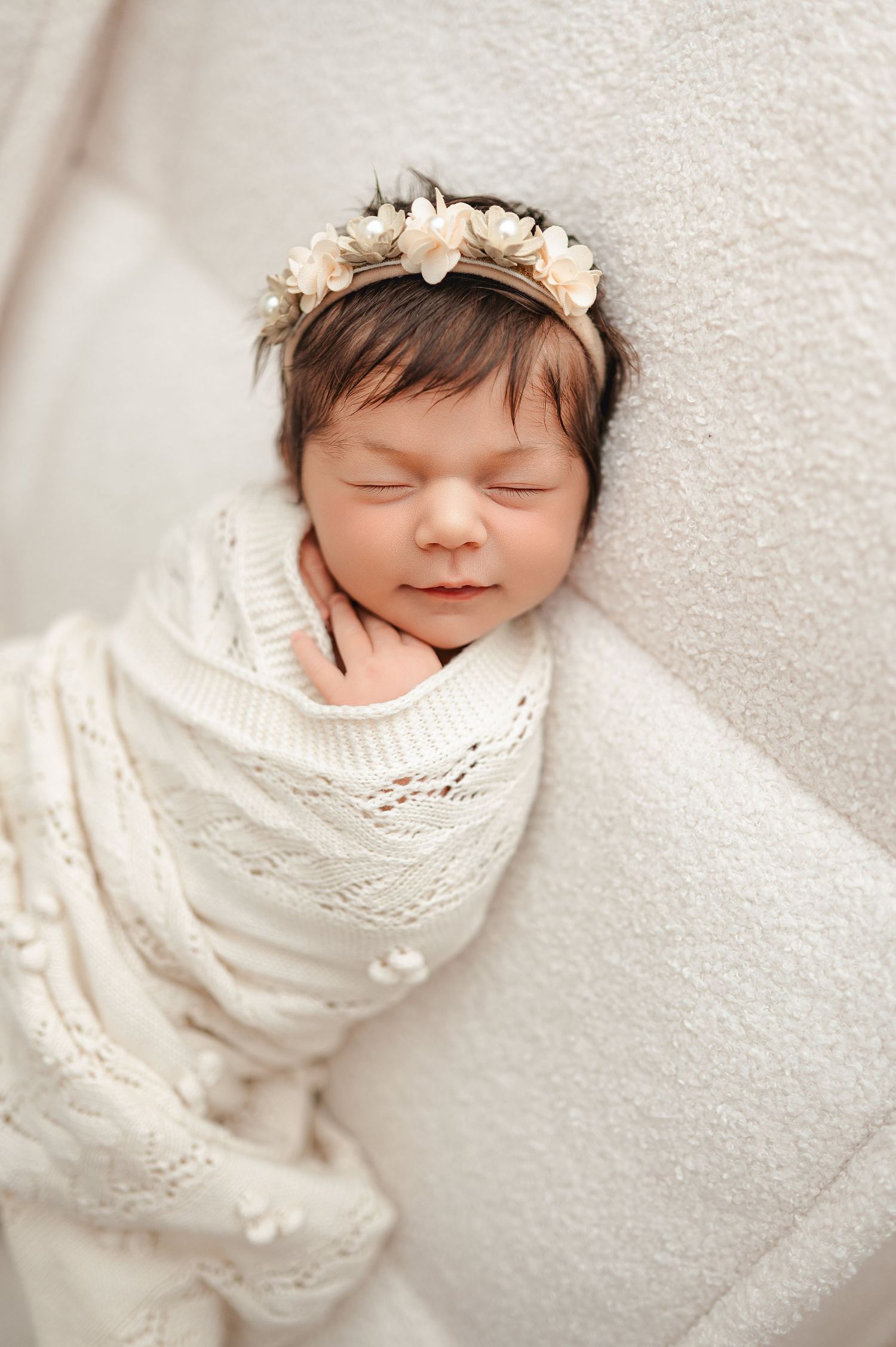 A sleeping newborn swaddled in white knitted wrap rests peacefully on soft white textured backdrop in series of photos.