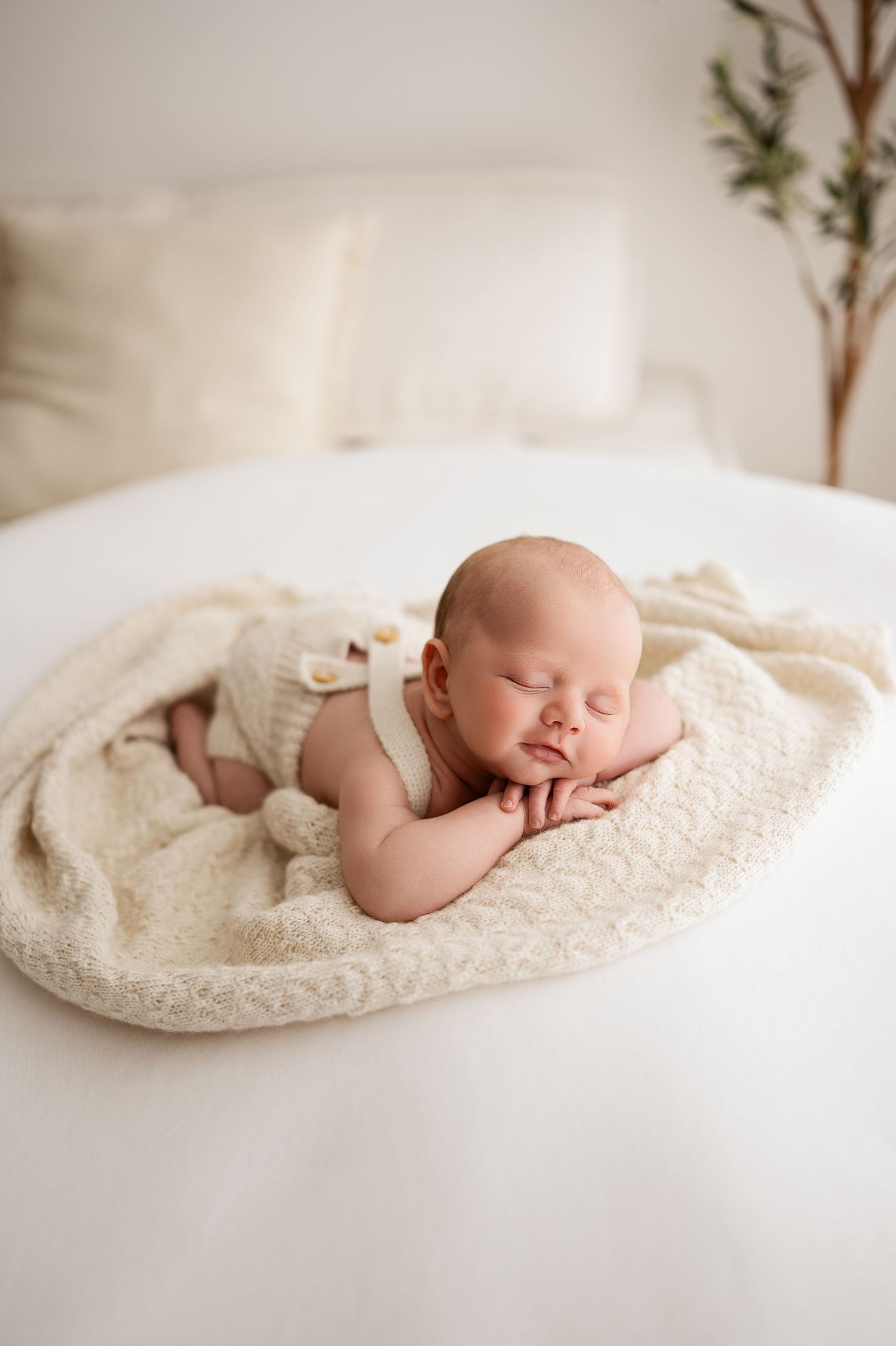 Newborn baby sleeping peacefully on soft white blanket in minimalist studio setting.
