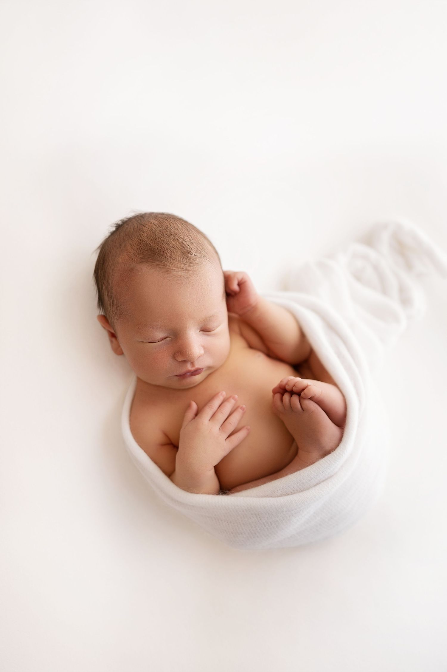 Peaceful sleeping newborn baby wrapped in soft white blanket during professional studio photography session.