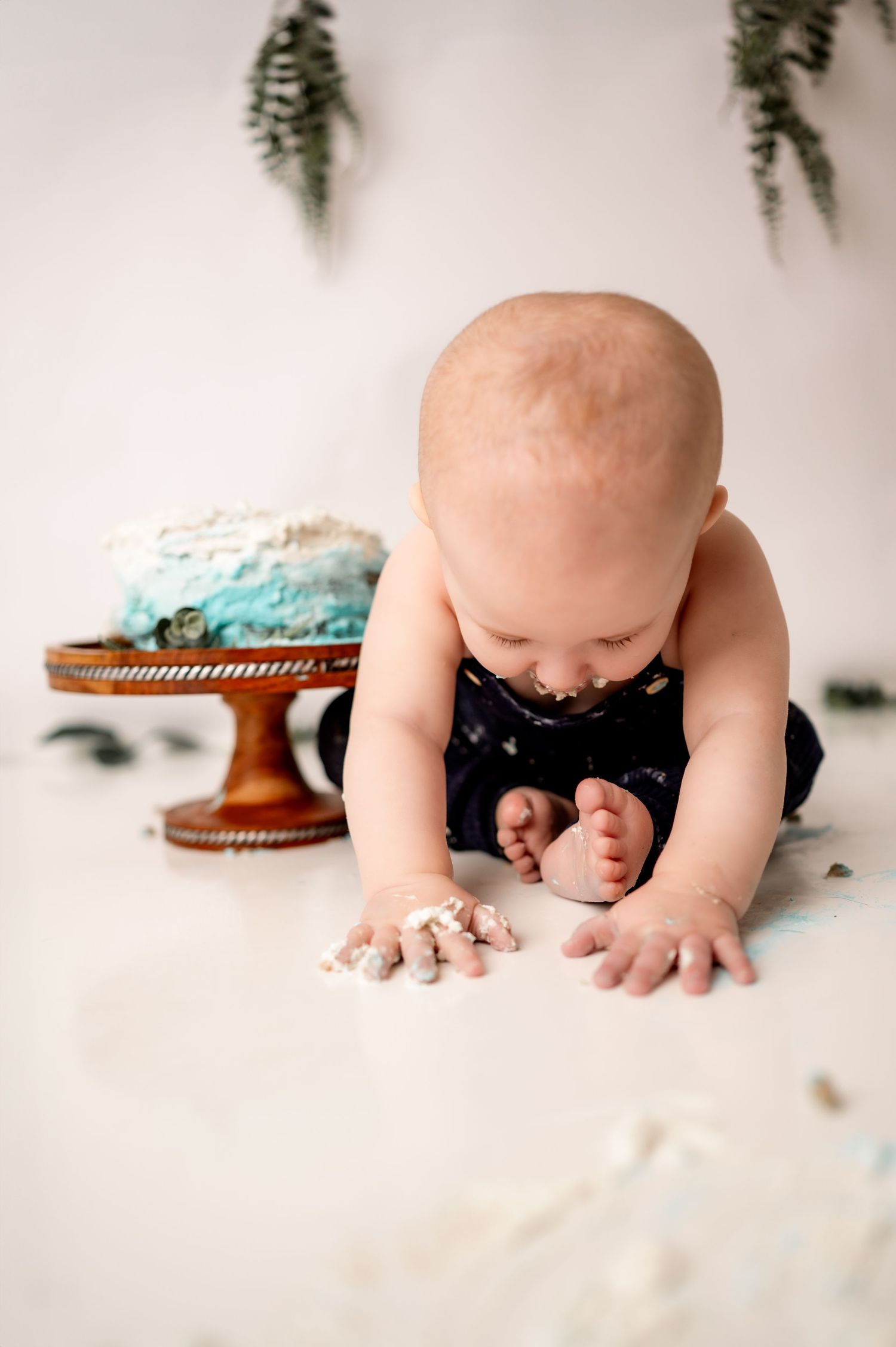 Baby crawls on white backdrop near scattered cake crumbs during a messy cake smash photography session.