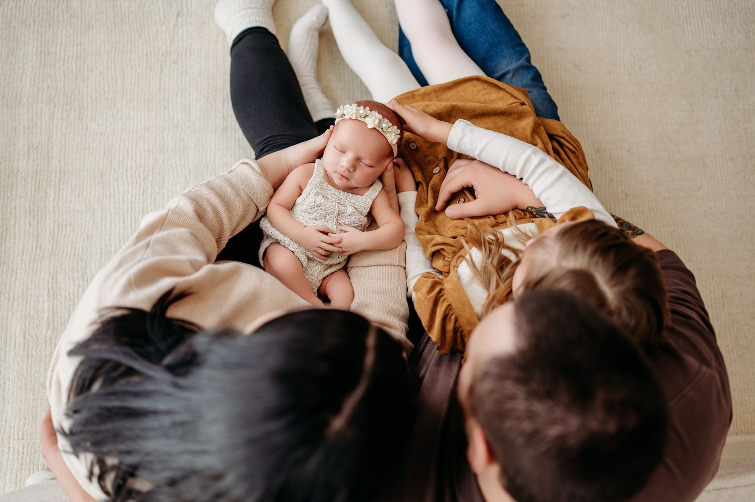 Bird's eye view of newborn baby lying between two adults on beige carpet during an intimate family portrait session.