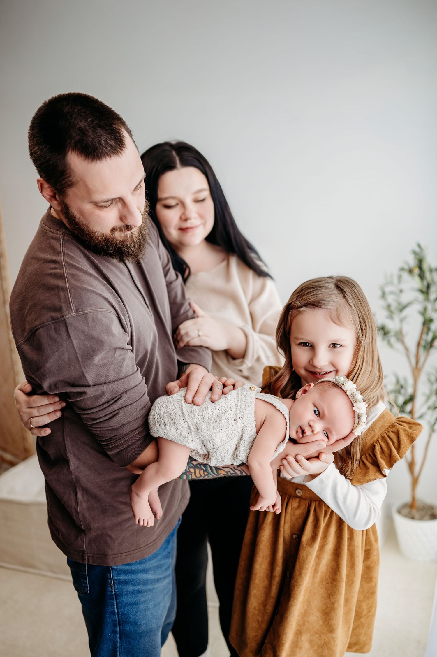 A family stands together indoors capturing a tender moment with their newborn baby in a bright, minimalist setting.