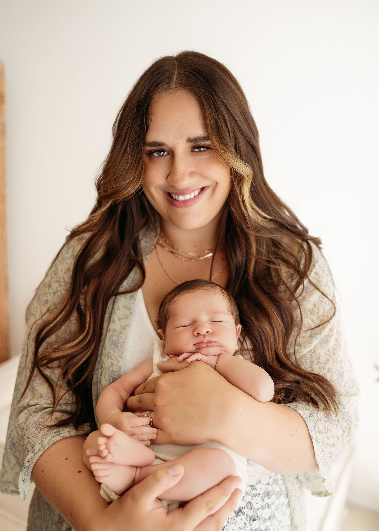 A tender portrait shows a peaceful sleeping newborn being gently cradled against a light background.