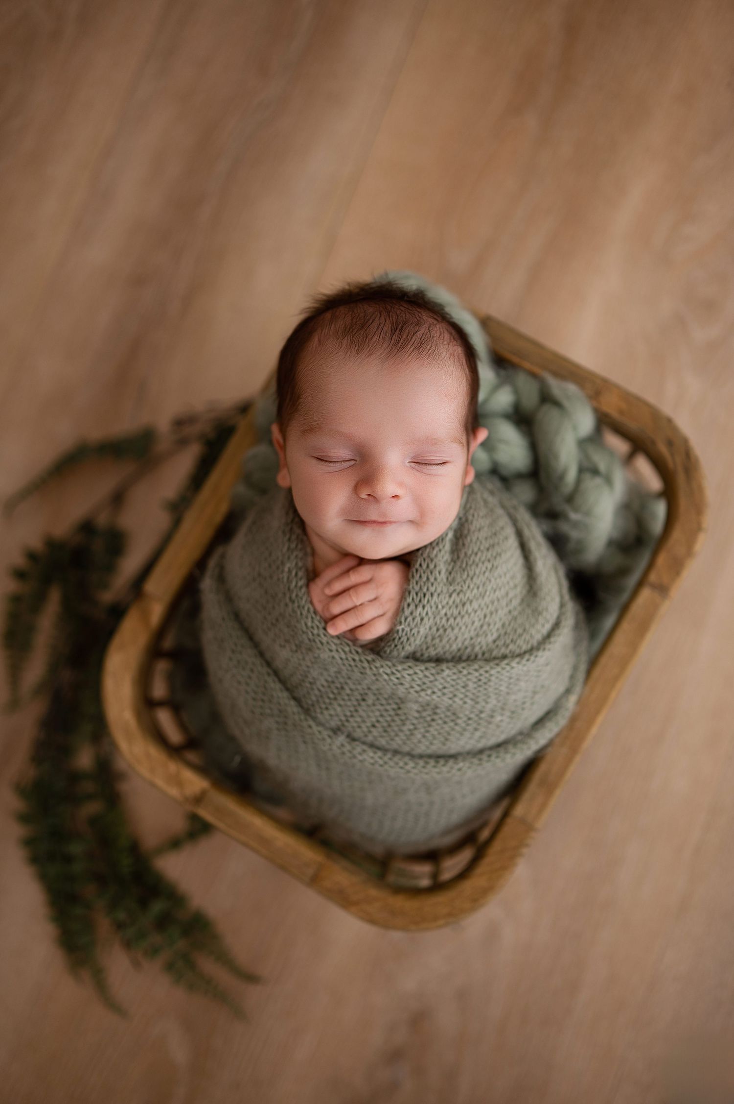 Sleeping baby wrapped in gray knit blanket in wooden bowl with rustic backdrop.