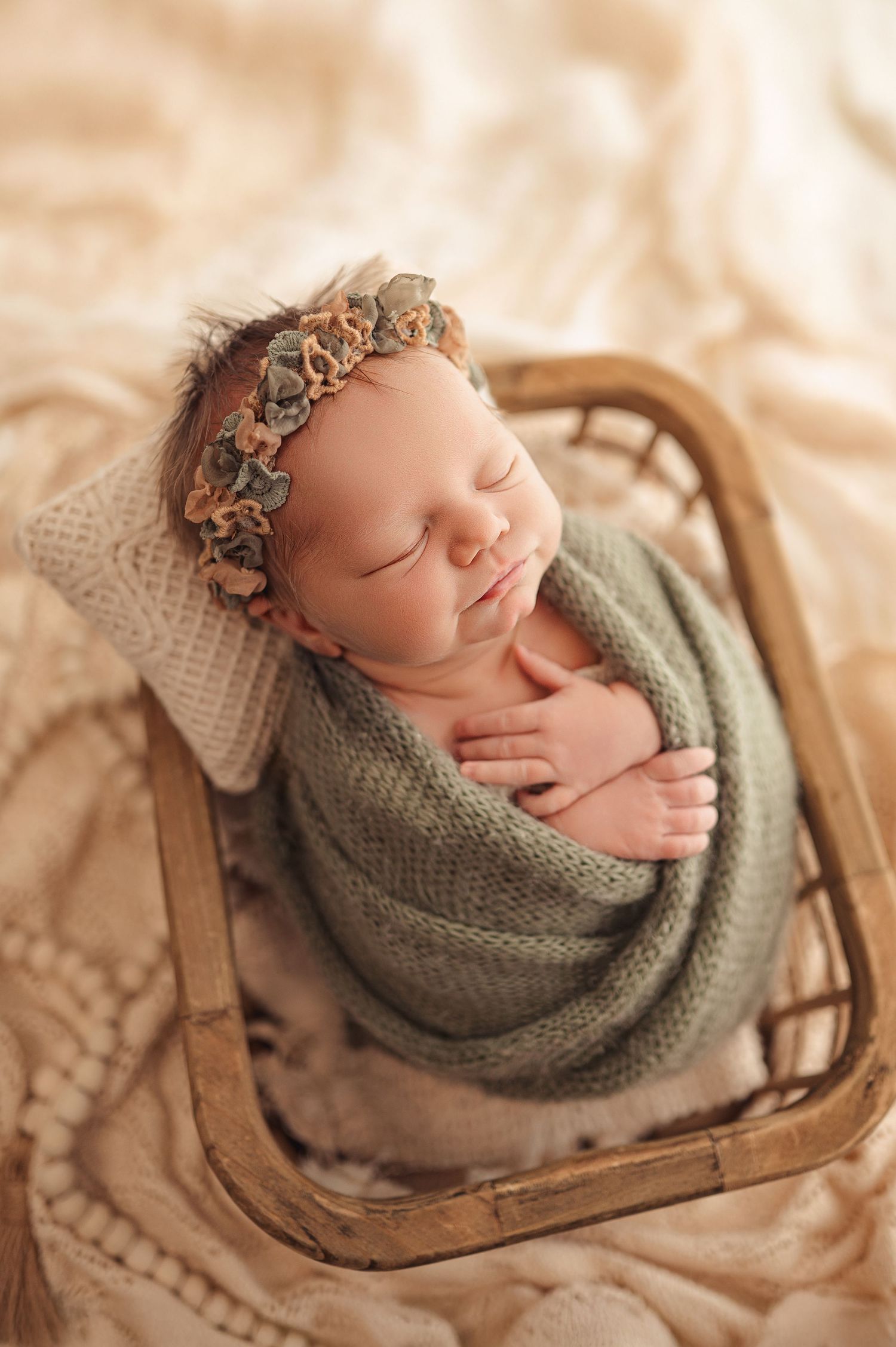 A sleeping newborn wrapped in a gray knit blanket rests peacefully in a rustic wooden drawer.