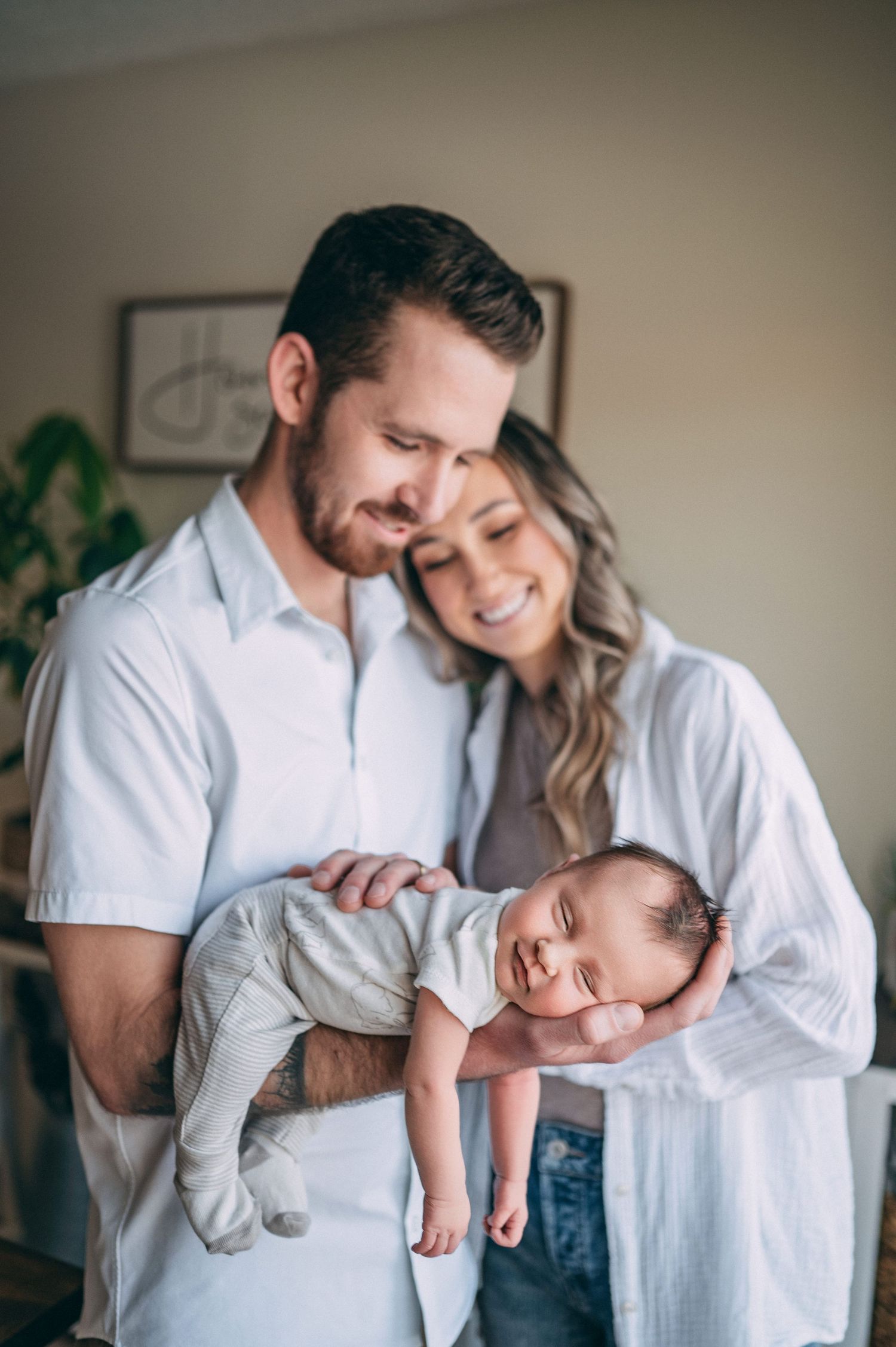 A tender family moment with a sleeping infant in gray clothing being held while standing indoors.