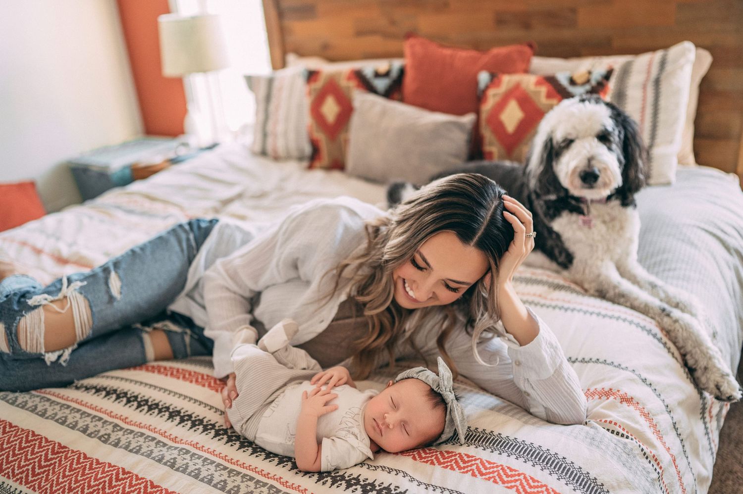 A cozy bedroom scene with someone resting on a patterned bedspread while a fluffy black and white dog looks on.