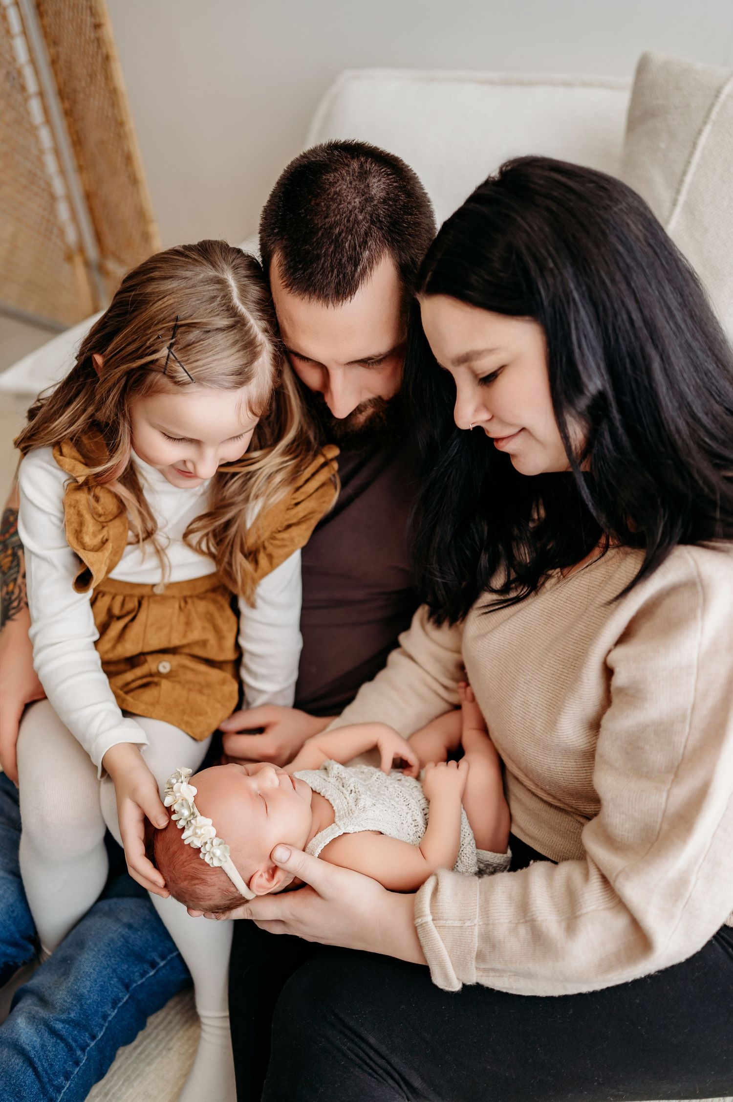 Family sitting together on couch shares intimate moment with new baby in cozy indoor setting.