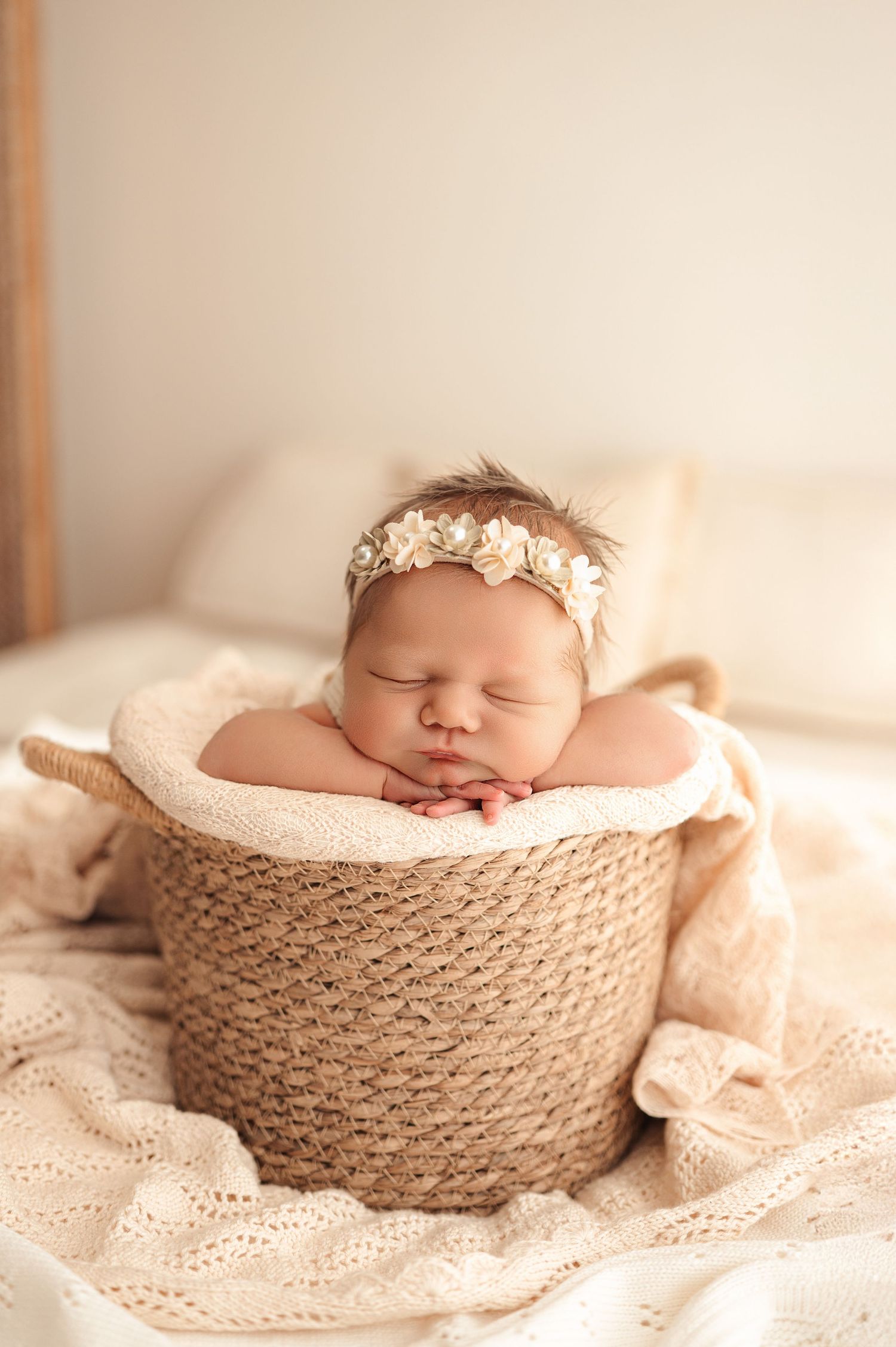 Sleeping newborn in tan woven basket nestled in soft cream knit blanket during professional photography session.