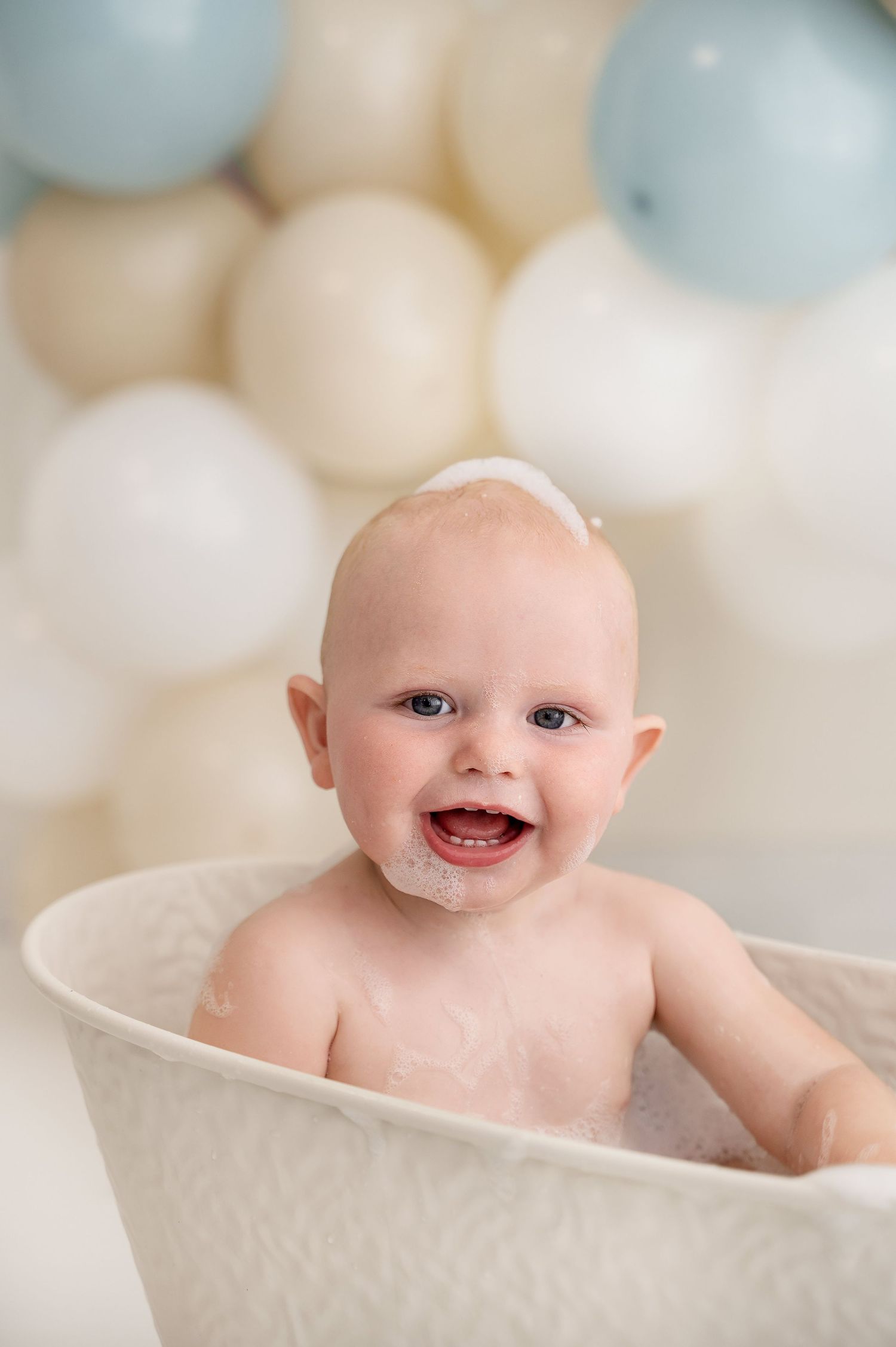 Baby enjoying bath time in white vintage tub with soft balloon background.