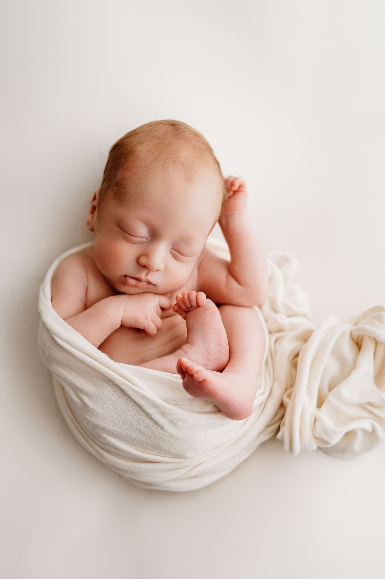 Sleeping newborn swaddled in soft white fabric against minimalist white background in three similar poses.
