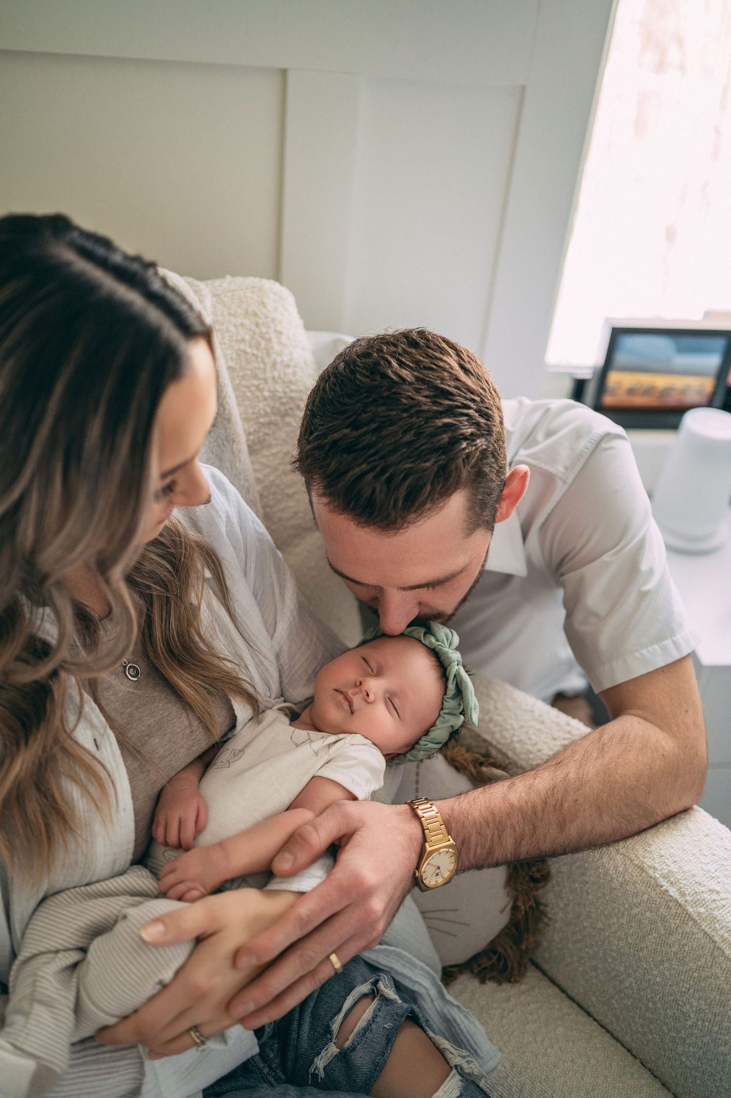 Intimate family moment with sleeping newborn on cream colored couch.